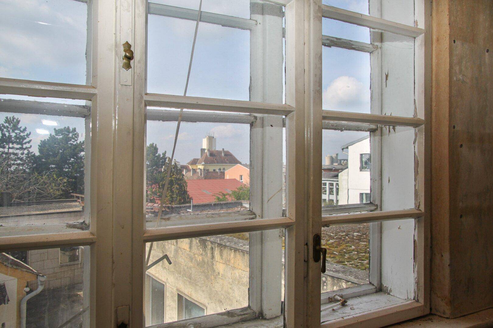 Blick aus einem alten Fenster mit Sprossen auf umliegende Dächer und Gebäude.