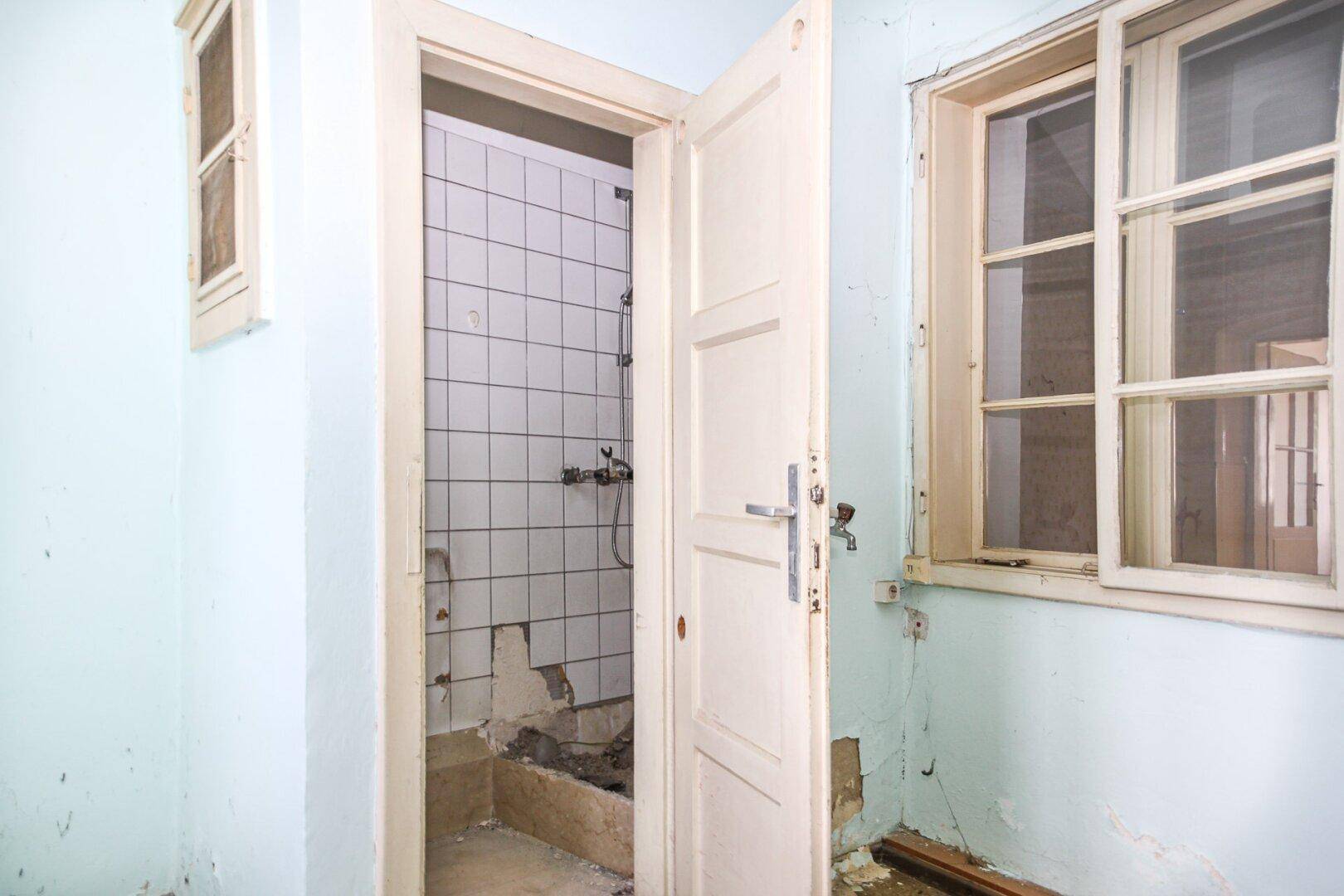 Kleines Badezimmer mit gefliestem Duschbereich und abgenutzten Wänden, stark renovierungsbedürftig.