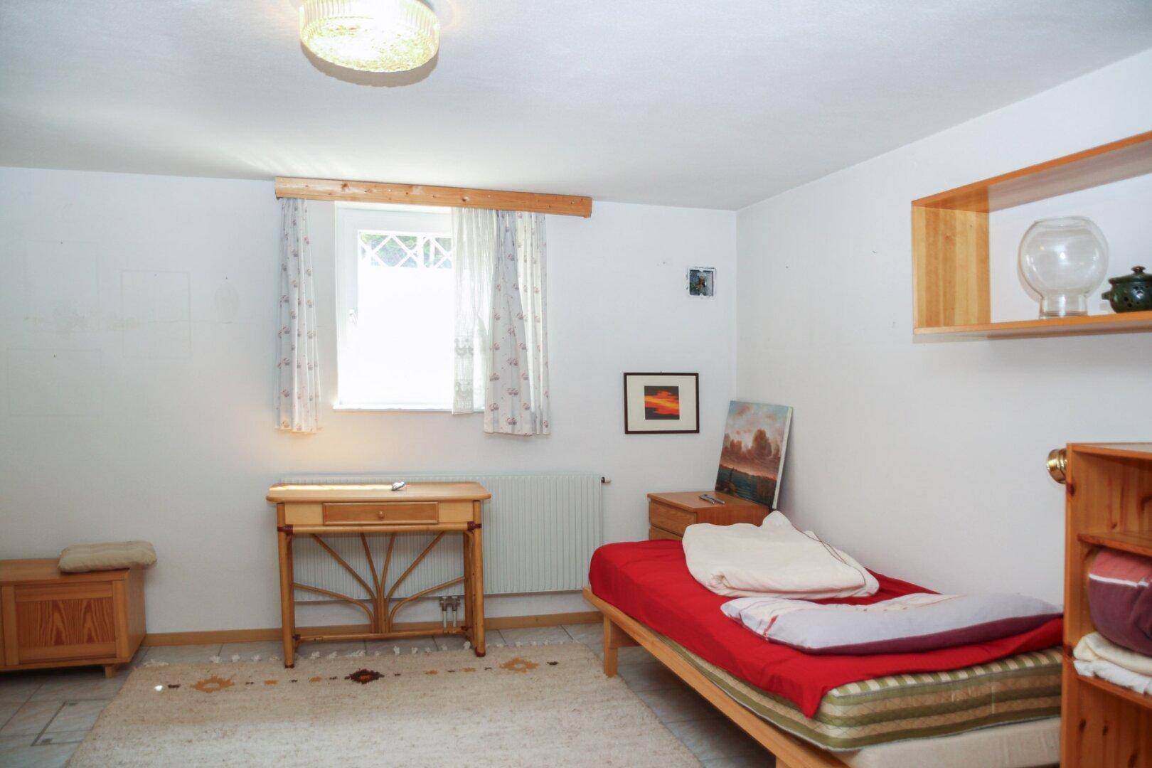 Schlichtes Schlafzimmer mit Einzelbett, Holzmöbeln und Fenster.