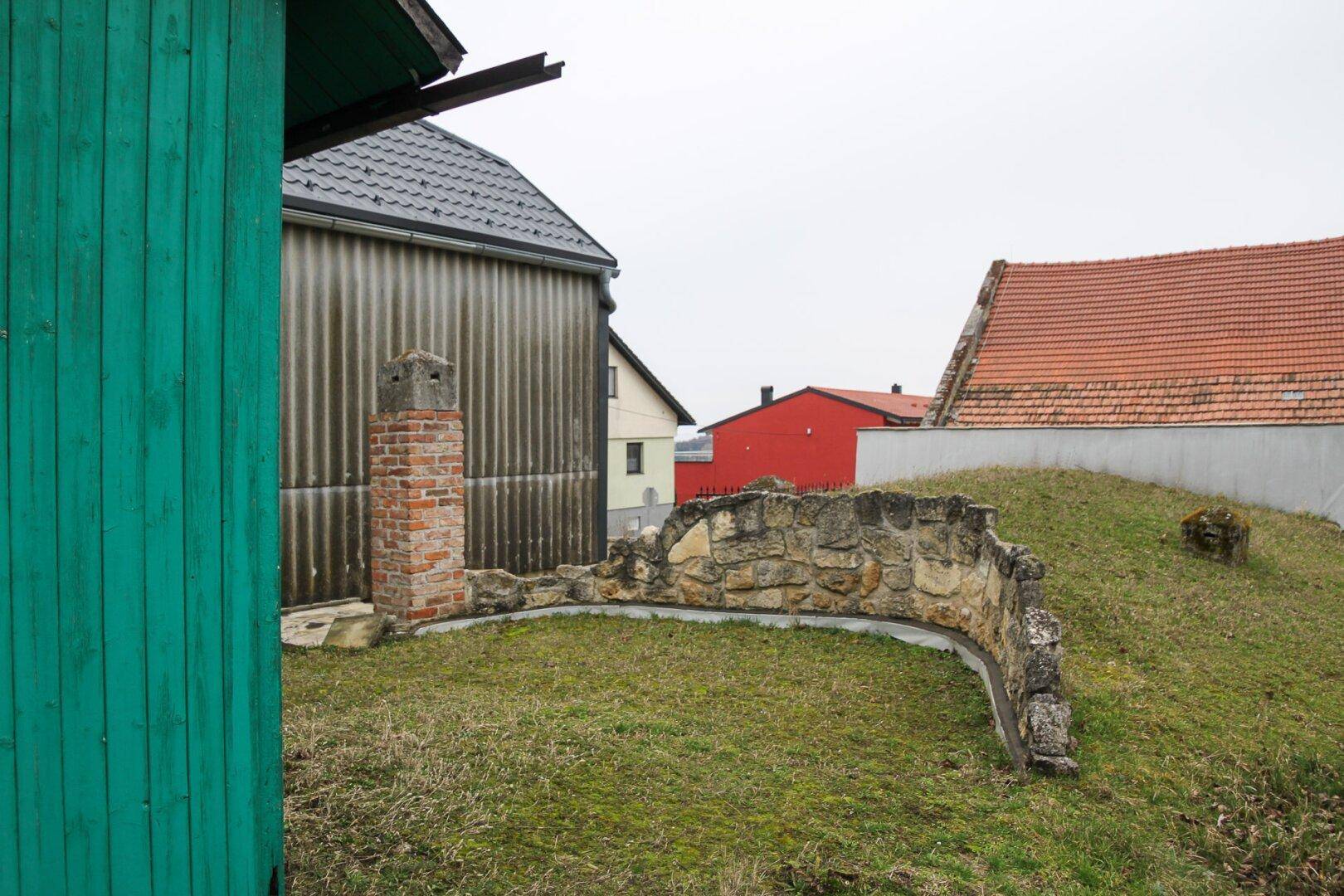 Gartenansicht mit Rasen, Steinmauer und Blick auf die umliegenden Gebäude und die hügelige Landschaft.