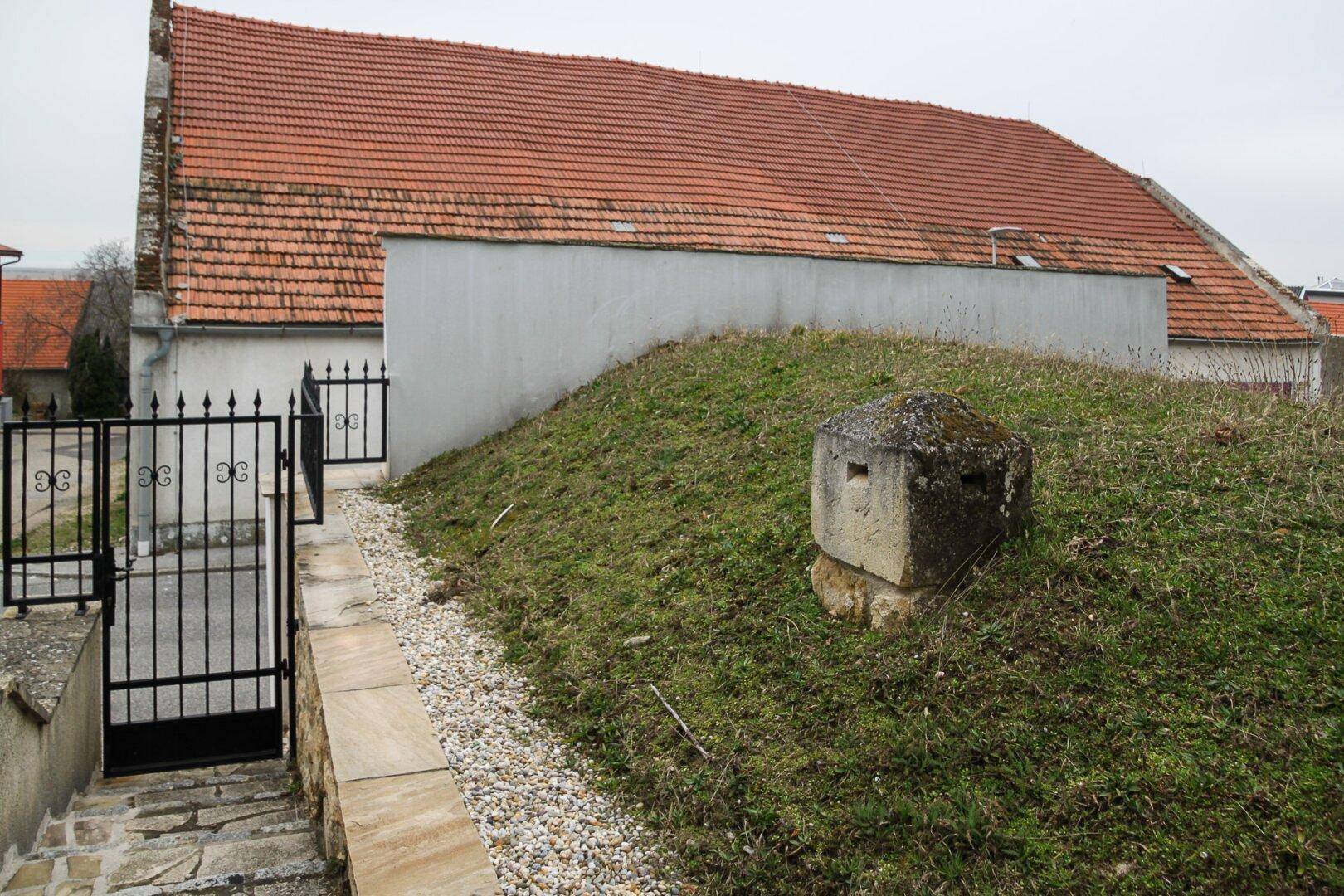 Gartenweg mit Kies und Steinplatten, umgeben von Rasen und einer kleinen Steinmauer mit Torzugang.