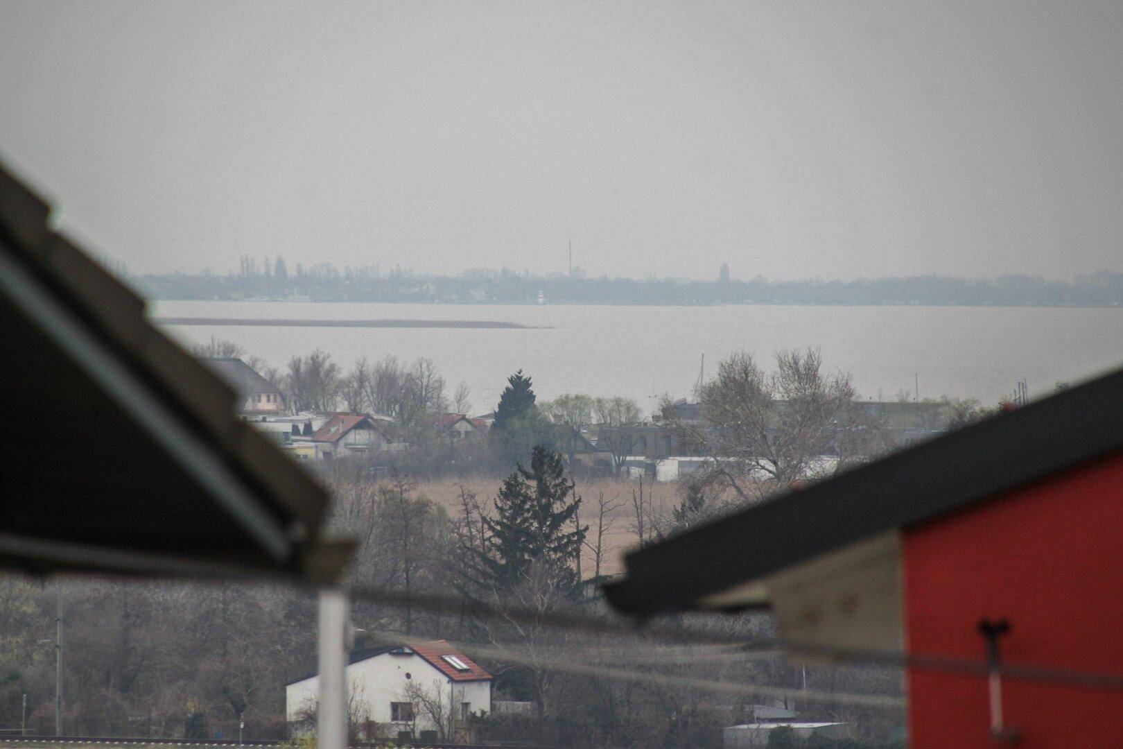 Panoramablick auf die weite Landschaft mit einem See und bewaldeten Ufern unter grauem Himmel.
