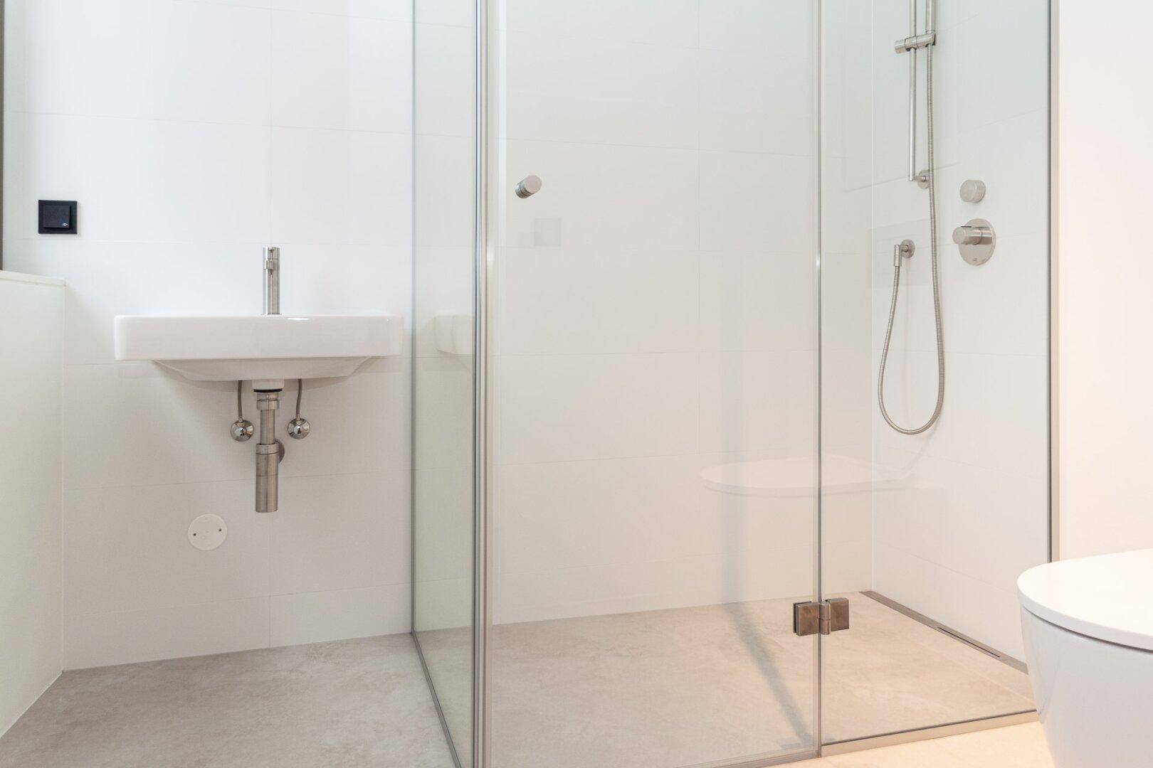 Modernes Badezimmer mit bodengleicher Dusche, minimalistischem Waschbecken und weißen Fliesen.