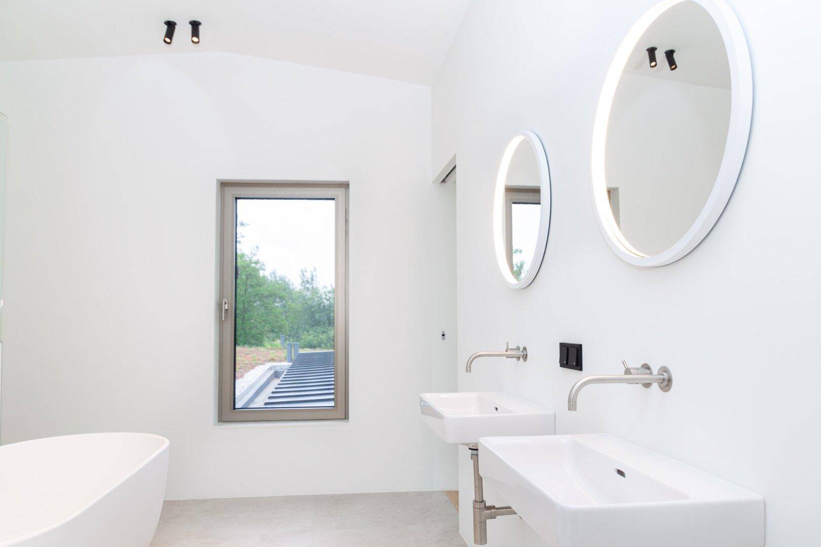 Helles Badezimmer mit zwei modernen Waschbecken, runden Spiegeln und einem Fenster.
