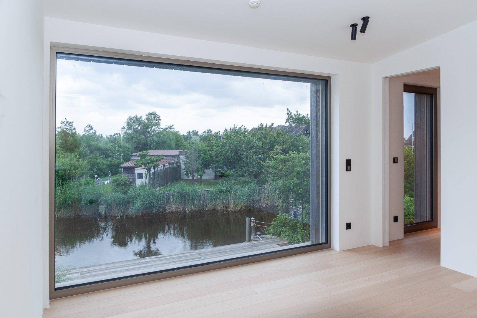 Heller Raum mit großer Fensterfront, die einen weiten Blick auf das Wasser und die grüne Umgebung ermöglicht.
