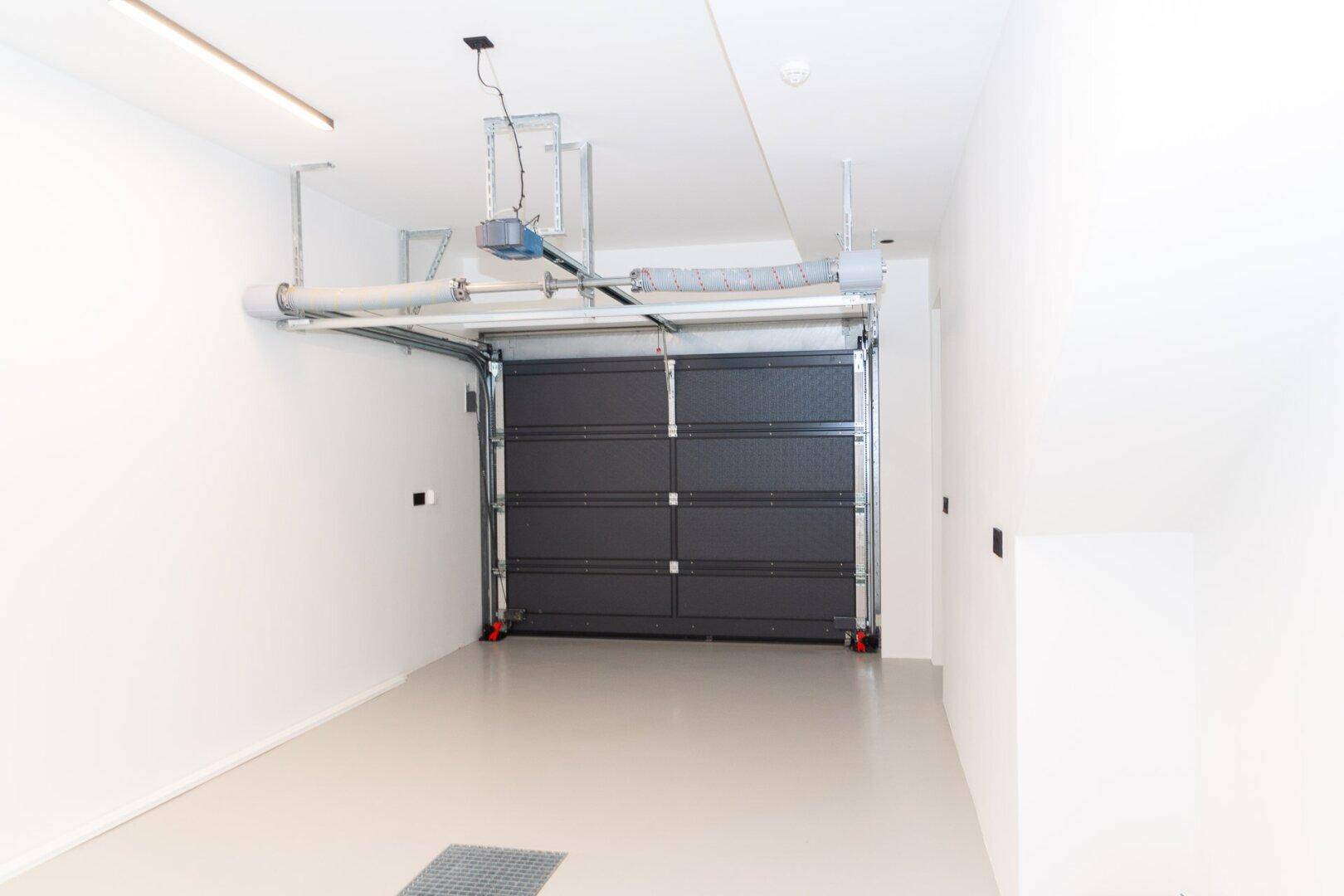 Saubere und helle Garage mit automatischem Garagentor und ausreichend Platz für ein Fahrzeug.