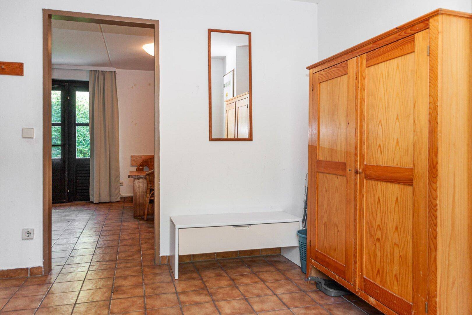 Einfacher Eingangsbereich mit Terrakottafliesen, Holzschrank und Spiegel.