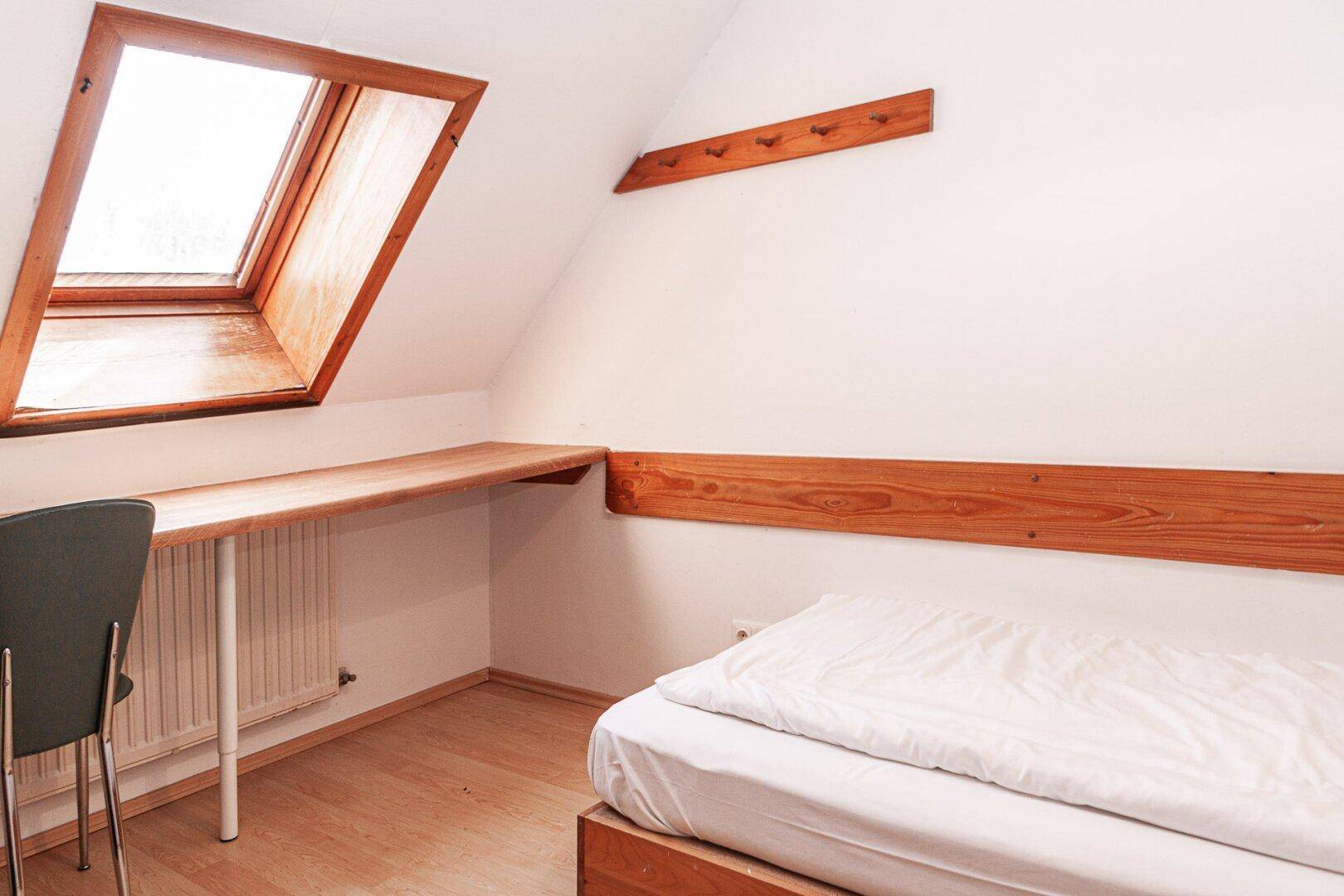Helles Schlafzimmer im Dachgeschoss mit Schreibtisch und Dachfenster.