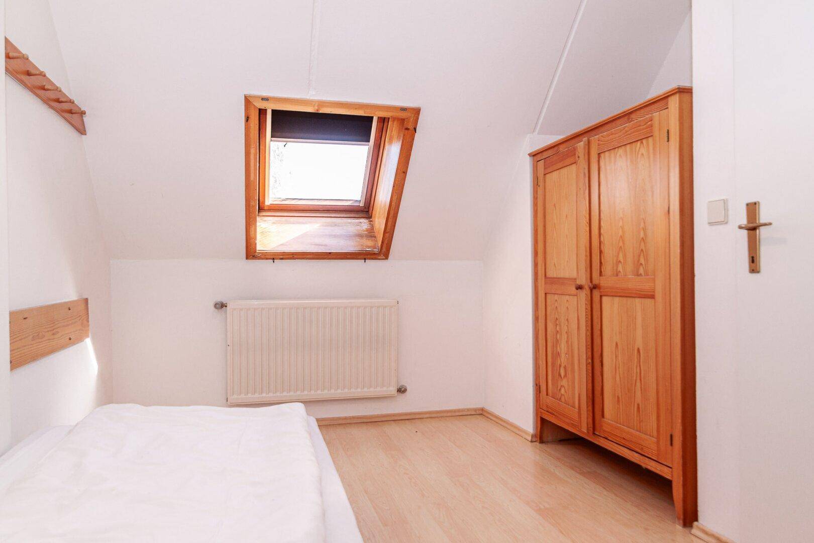 Schlafzimmer mit Holzkleiderschrank, Einzelbett und Dachfenster.
