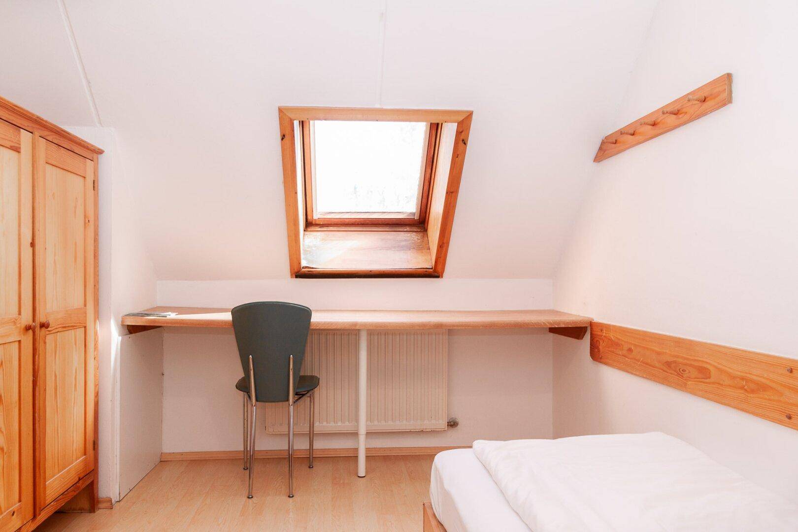Schlafzimmer mit Dachfenster, Schreibtisch und Holzbett in heller Umgebung.