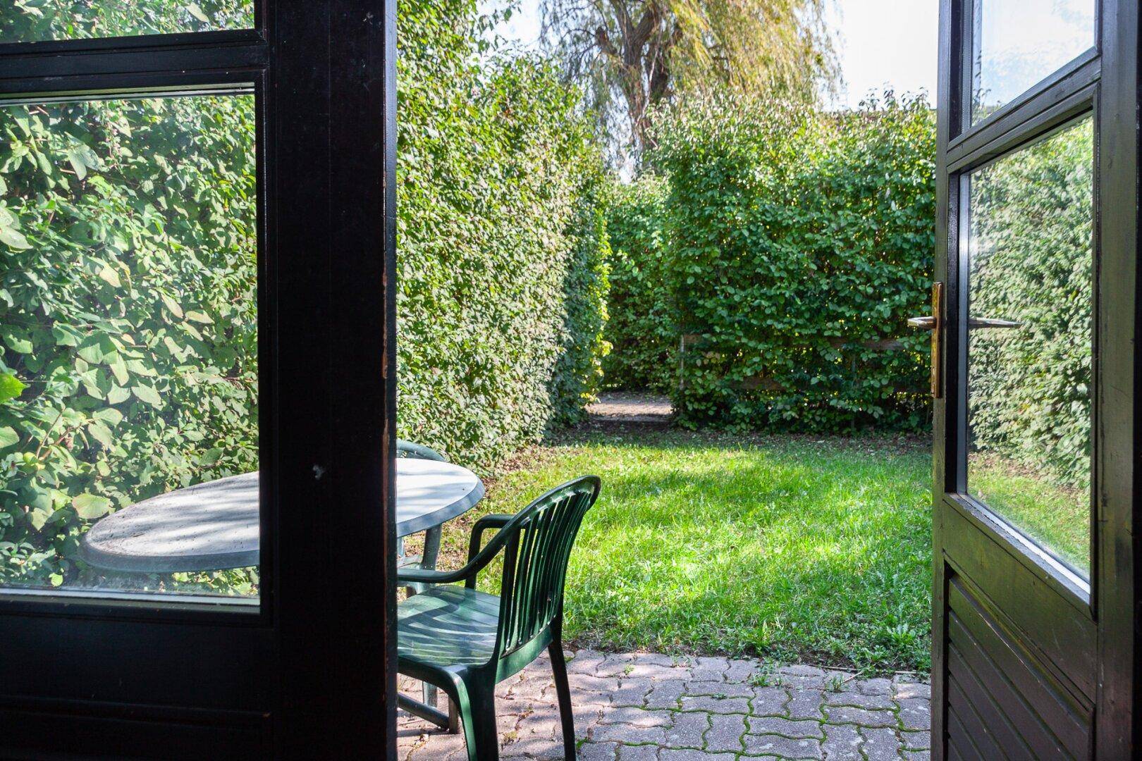 Kleiner Gartenbereich mit Terrasse, Gartenmöbeln und hohen Hecken.