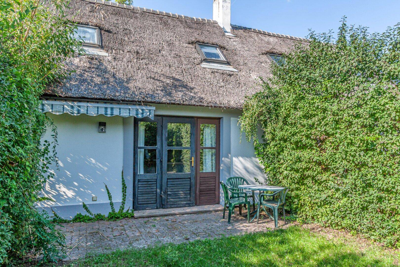 Rückseite des Hauses mit kleiner Terrasse, Gartenmöbeln und Reetdach.