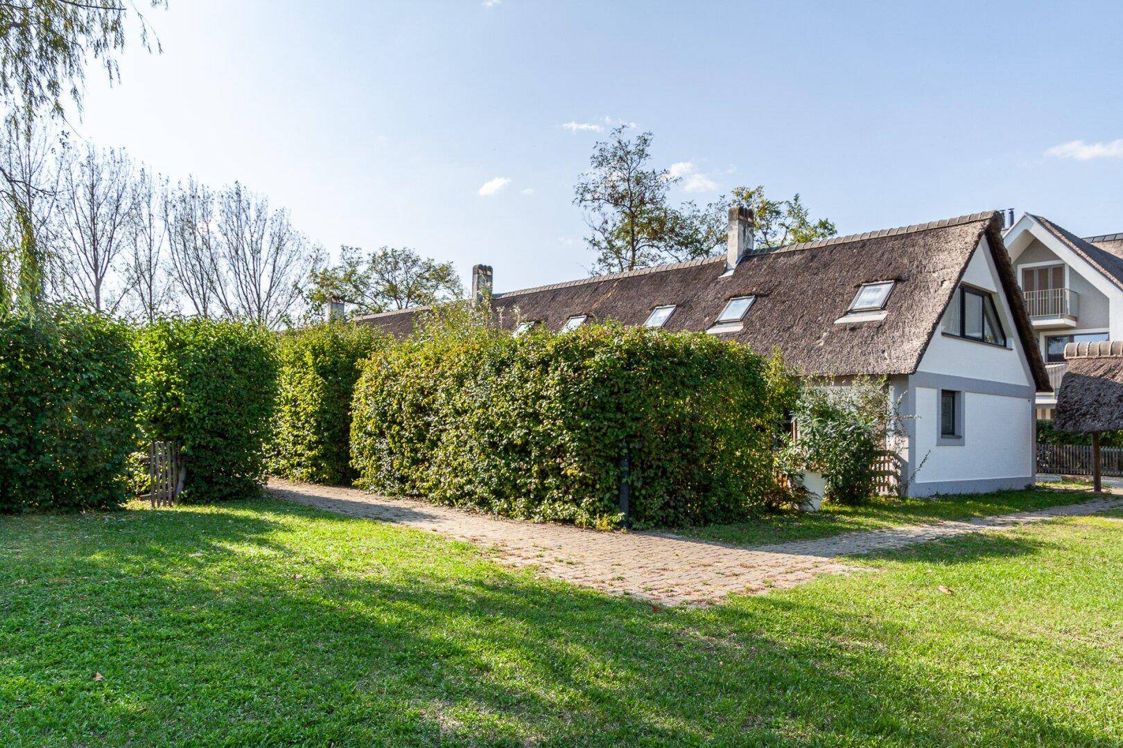 Weitläufiger Gartenbereich mit Rasenflächen und traditionellen Reetdachhäusern.