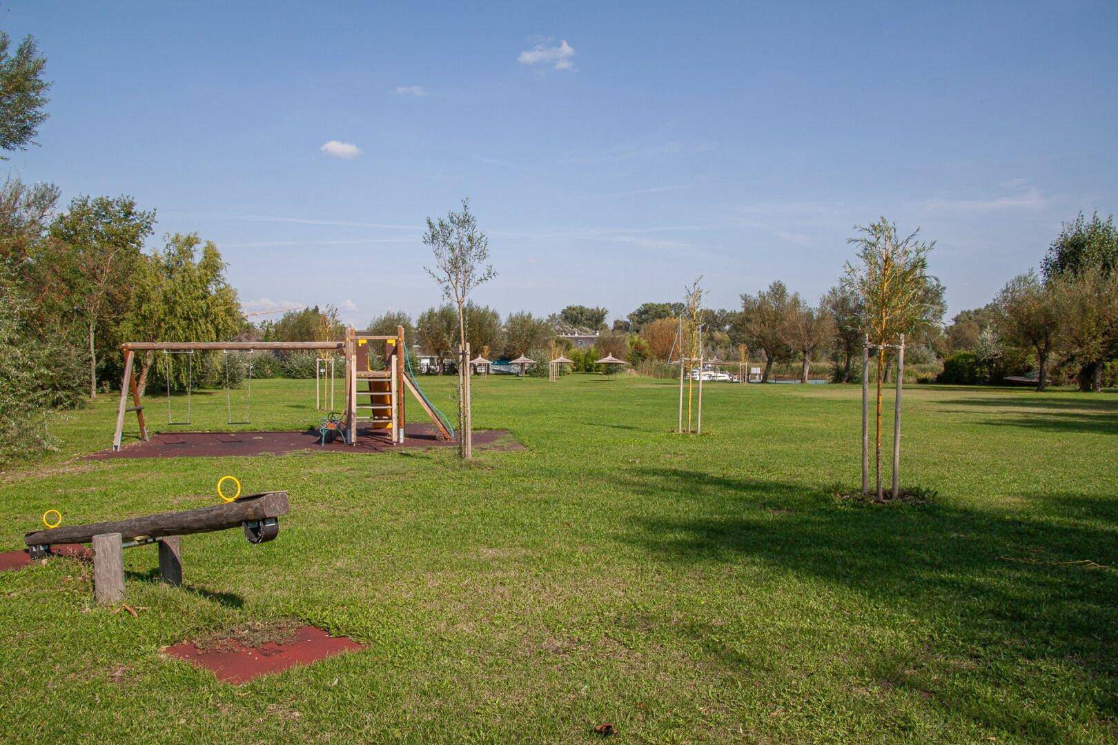 Großer Spielplatz mit Schaukeln und Rutsche auf einer weitläufigen Rasenfläche.