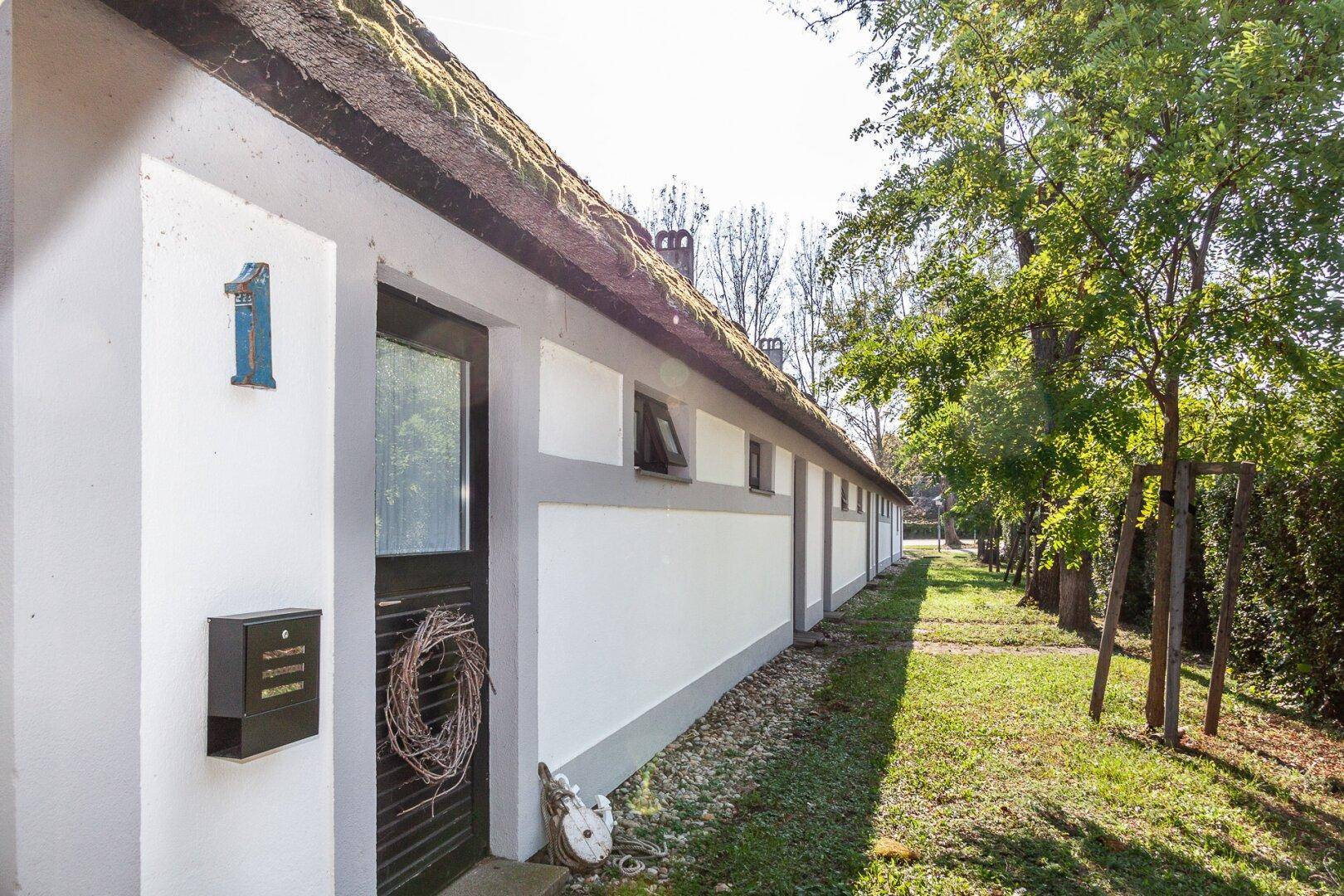 Seitenansicht eines Hauses mit Reetdach und Eingangstür.