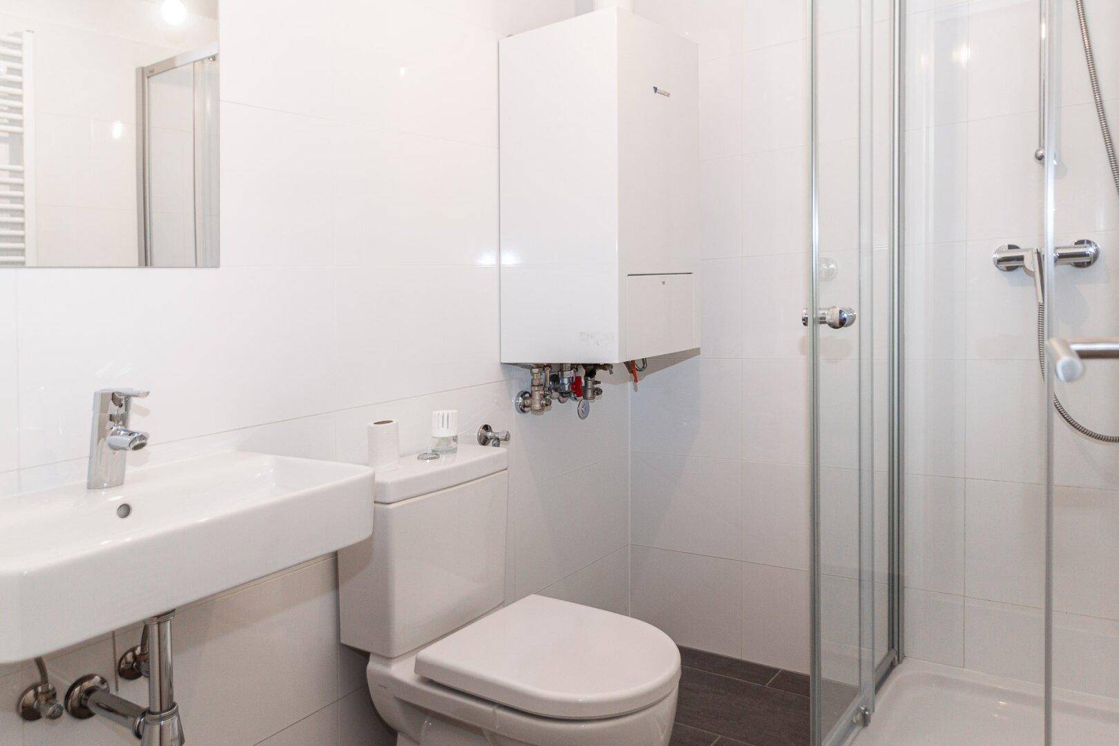 Modernes Badezimmer mit Dusche, WC, Waschbecken und weiß gefliesten Wänden und dunklem Boden.