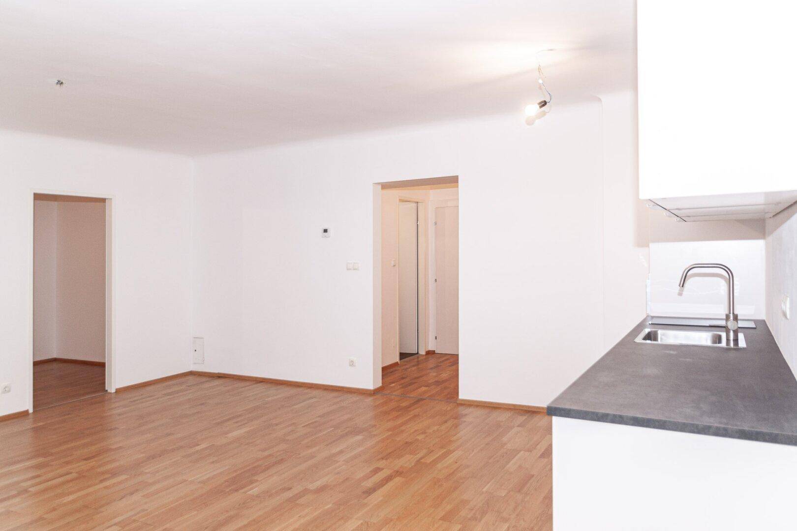 Geräumiger, heller Wohnbereich mit Holzfußboden und Zugang zu weiteren Zimmern der Wohnung.