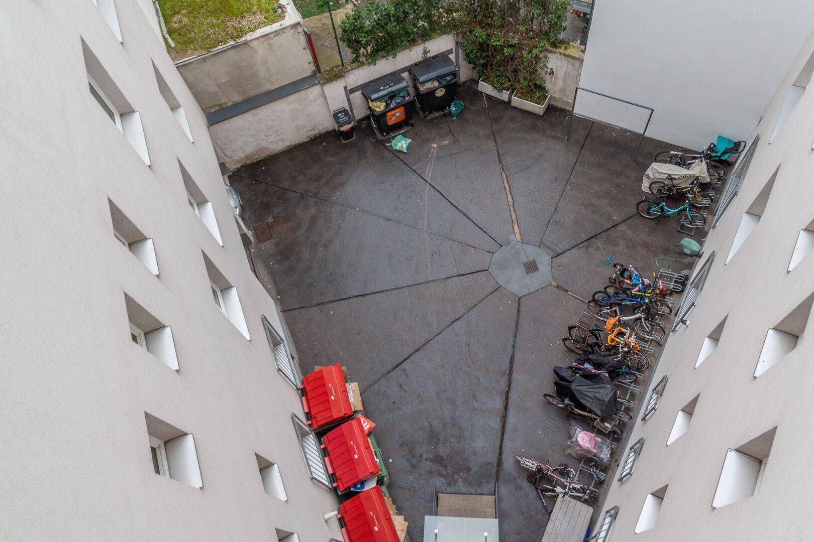 Blick von oben auf einen Innenhof mit Fahrradabstellplätzen und Mülltonnen.