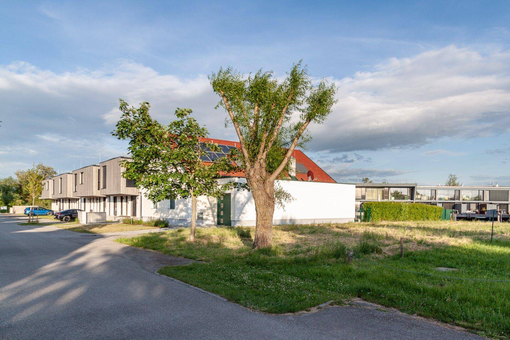 Mehrere Gebäude mit unterschiedlichen Dachtypen, darunter ein Haus mit Solaranlage und rotem Ziegeldach.