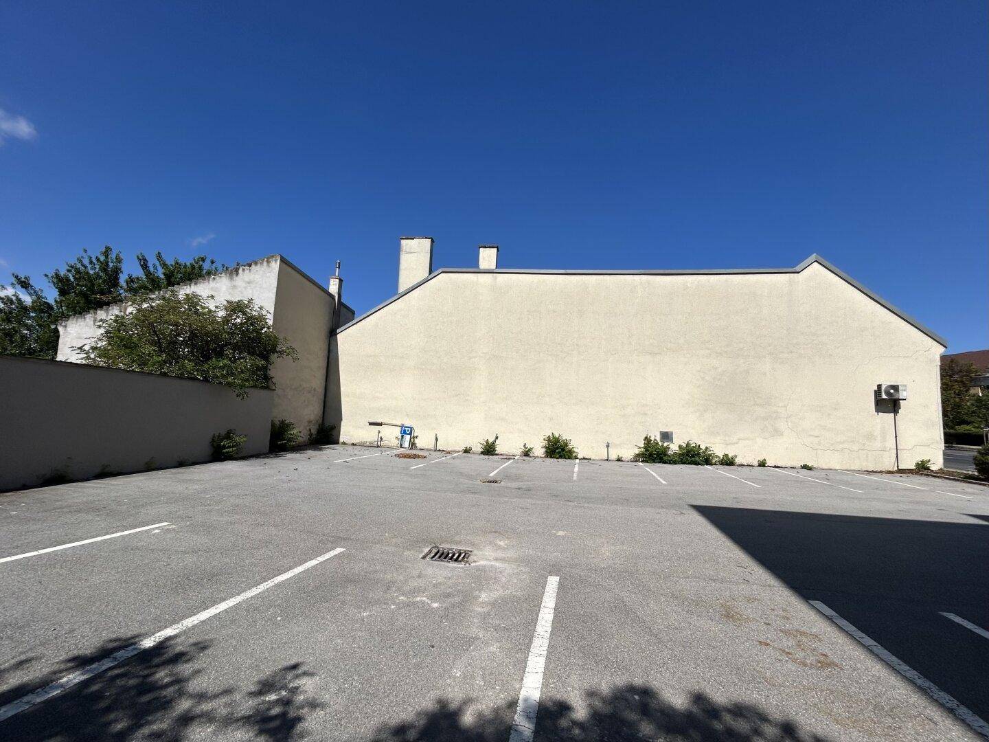 Gebäudeseite mit großem, leeren Parkplatz unter klarem, blauem Himmel an einem sonnigen Tag.