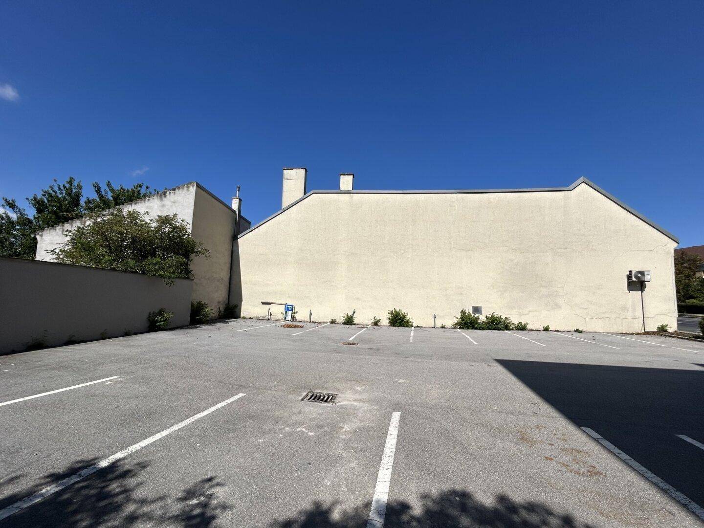Großer, leerer Außenparkplatz neben einem Gebäude mit schlichter Fassade unter klarem Himmel.