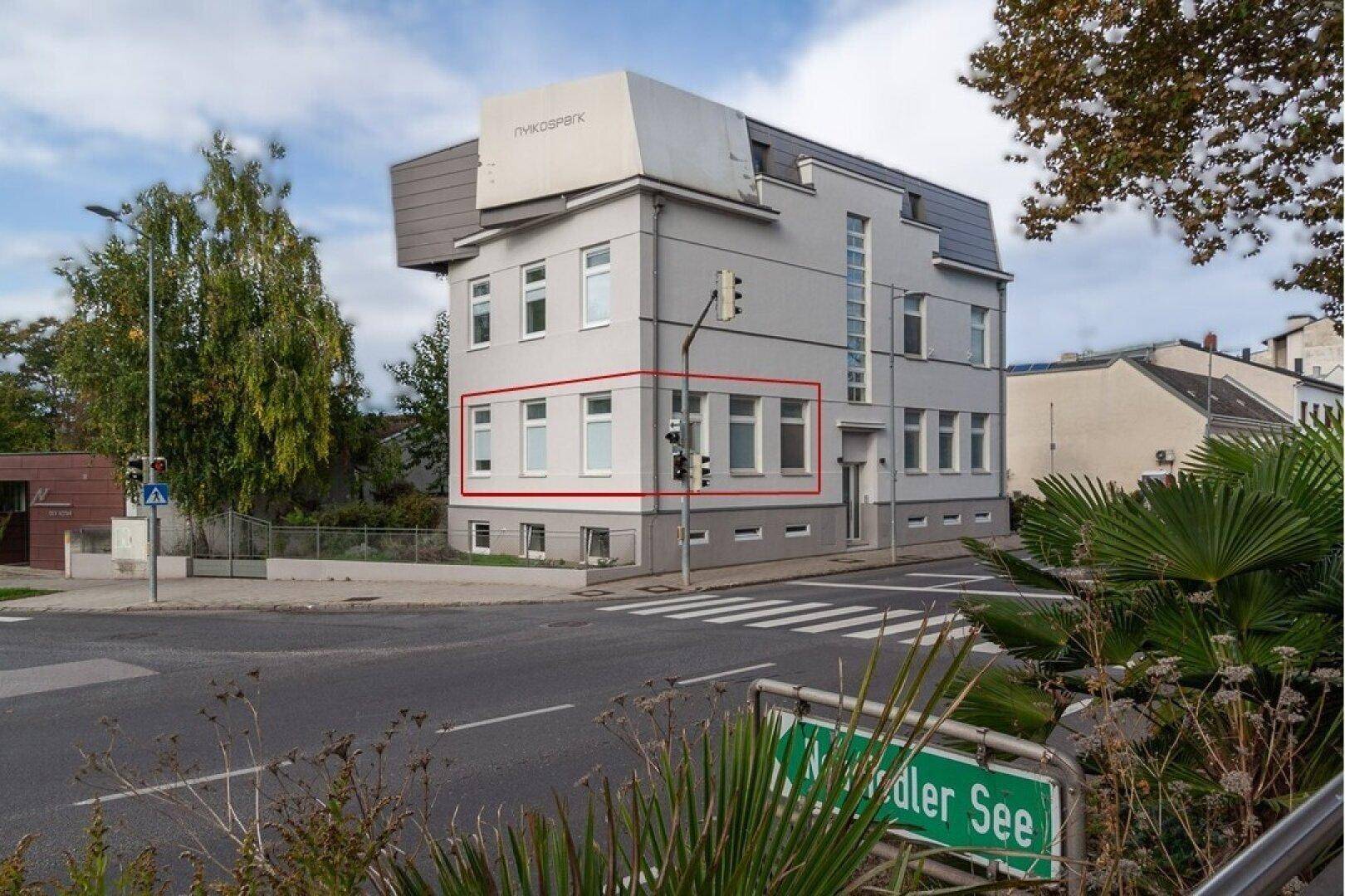 Modernes Gebäude an einer Straßenecke mit grauer Fassade und großen Fenstern, nahe dem Mödlinger See.