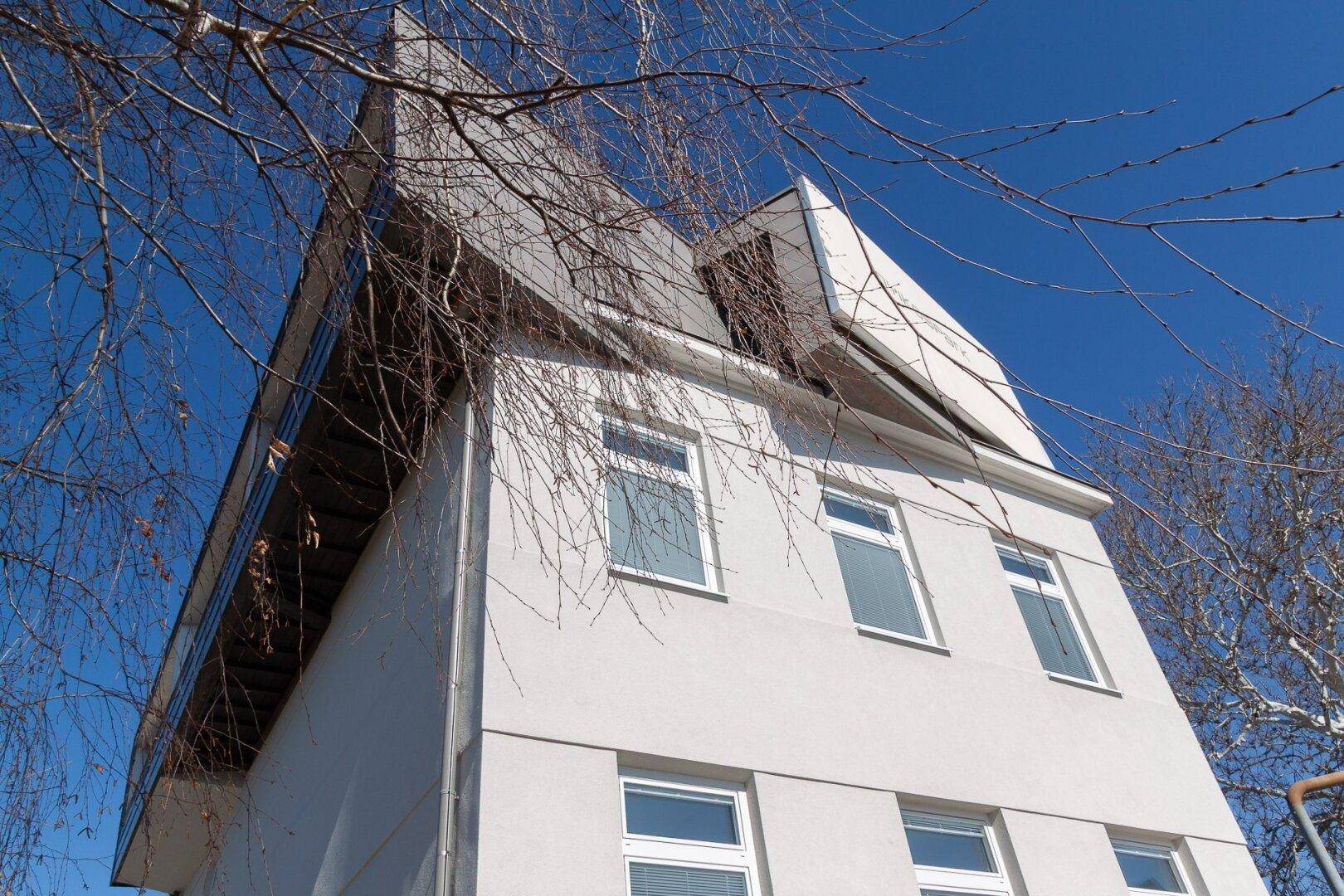 Detailansicht der modernen Gebäudefassade mit markanter Dachform unter blauem Himmel.