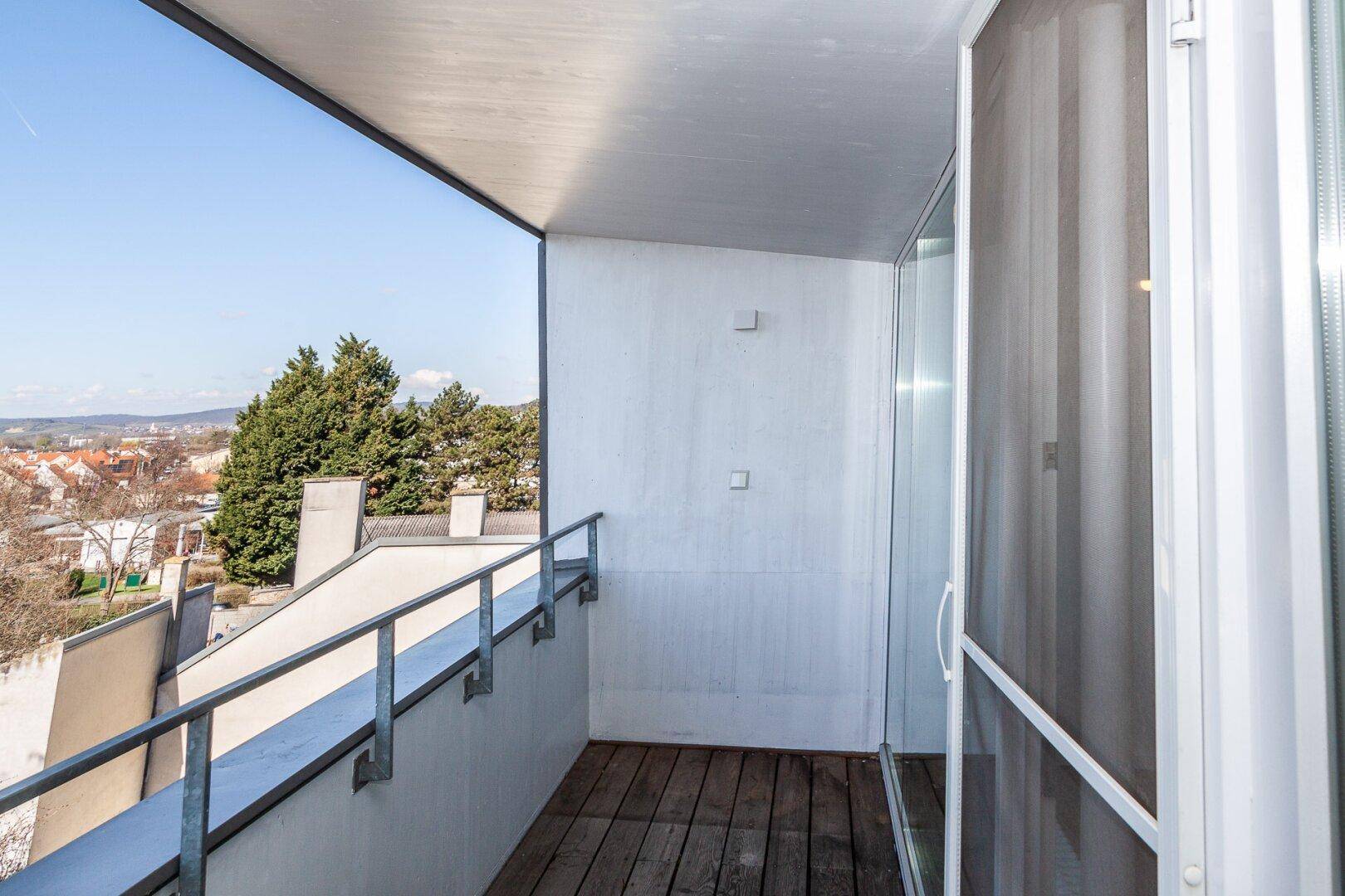 Schmaler Balkon mit Holzboden und weitem Blick über die Dächer und die hügelige Landschaft.