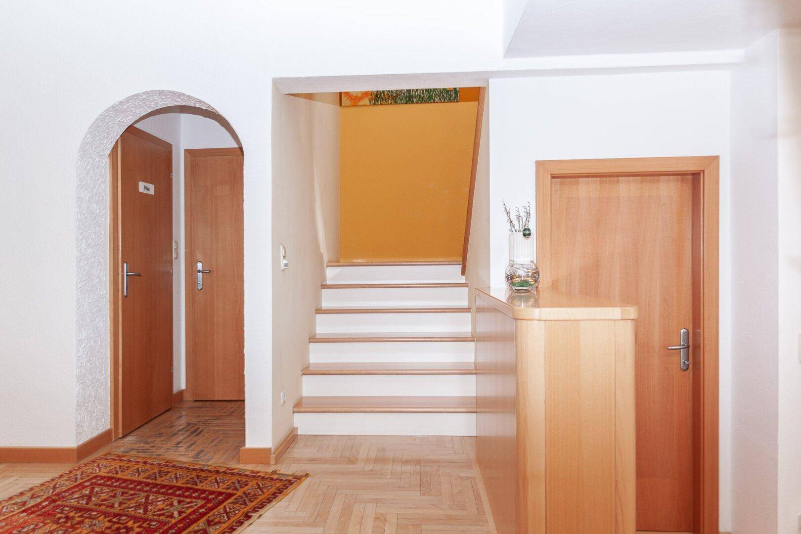 Eingangsbereich mit Holztreppe, Parkettboden und einem traditionellen Teppich.