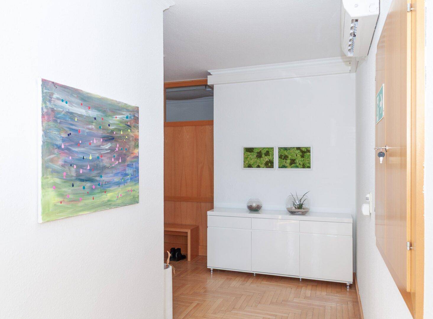 Moderner Flur mit weißem Sideboard, farbenfrohem Kunstwerk und Holzparkettboden.