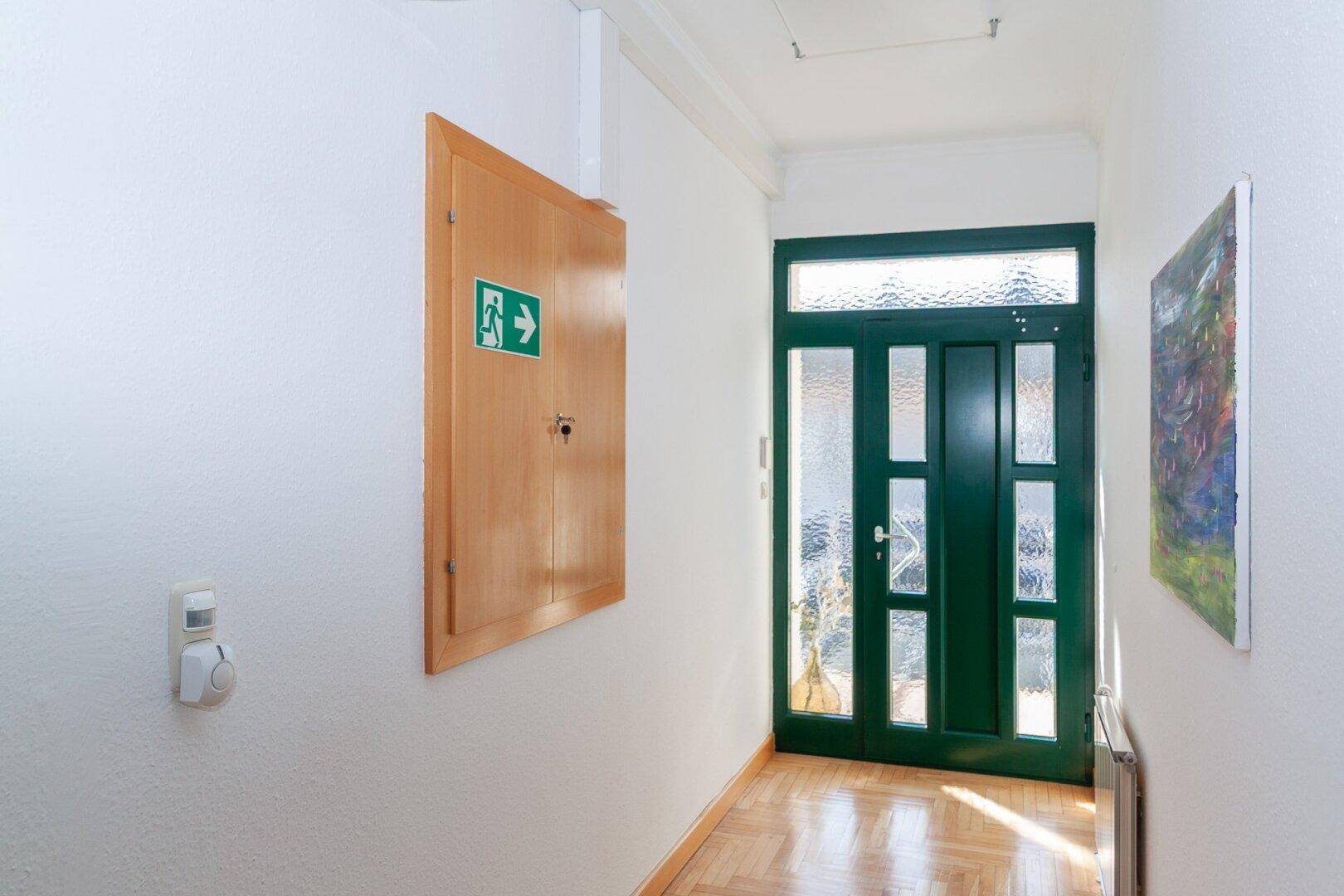 Heller Flur mit grüner Eingangstür, Holzparkettboden und einem Schrank an der Wand.