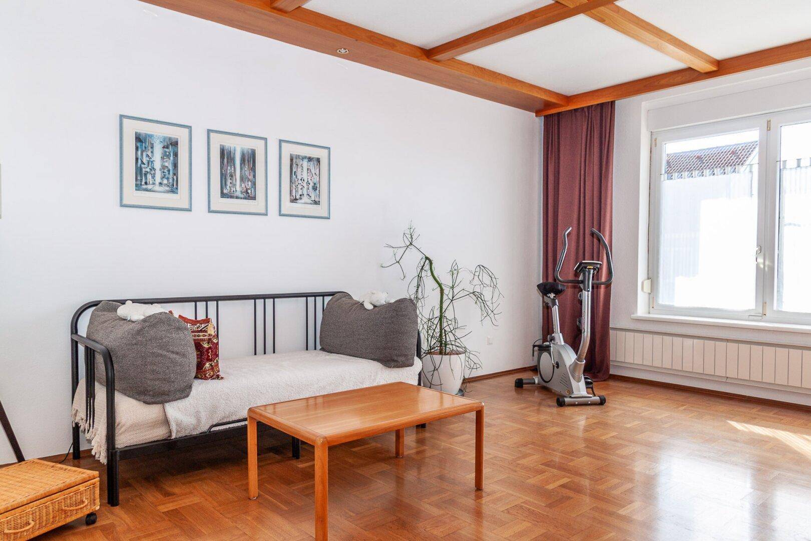 Helles Wohnzimmer mit Holzbalkendecke, Parkettboden und einem Tagesbett.