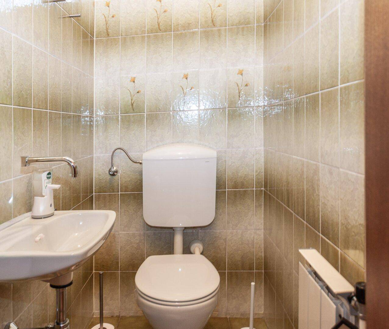 Kleines Gäste-WC mit beigefarbenen Fliesen, wandmontiertem WC und Einzelwaschbecken.