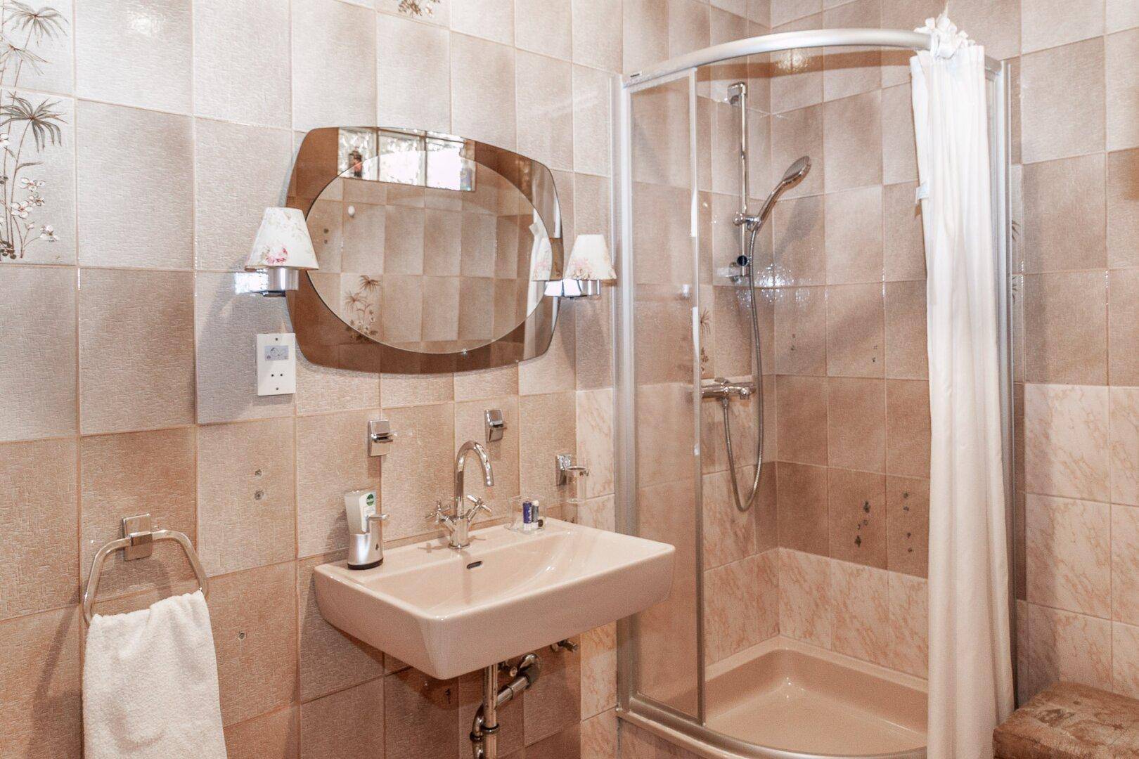 Badezimmer mit Duschkabine, Waschbecken und Spiegel, ausgestattet mit beigefarbenen Fliesen.