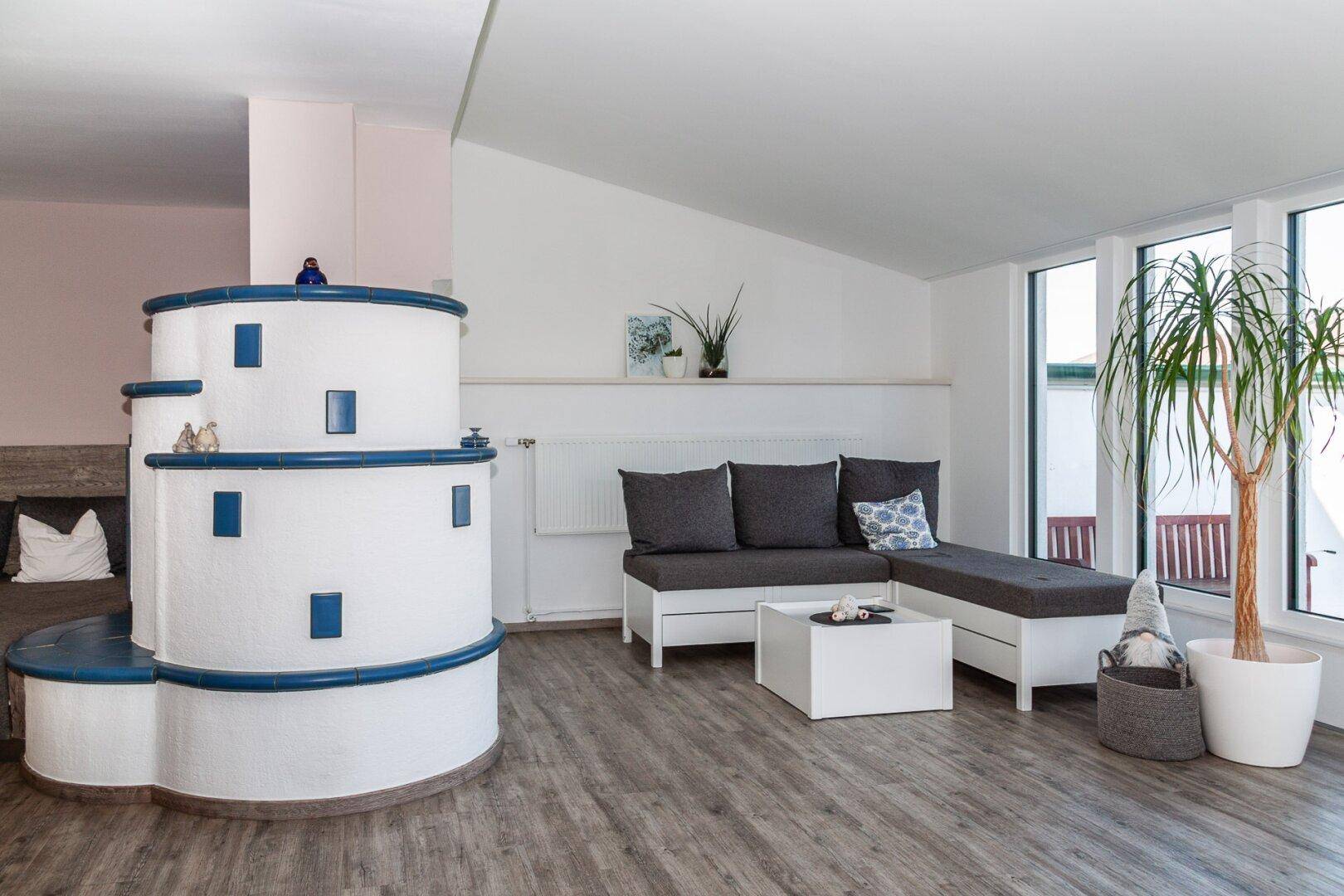 Gemütliches Wohnzimmer mit modernem Kachelofen, bequemer Sitzecke und großen Fenstern.