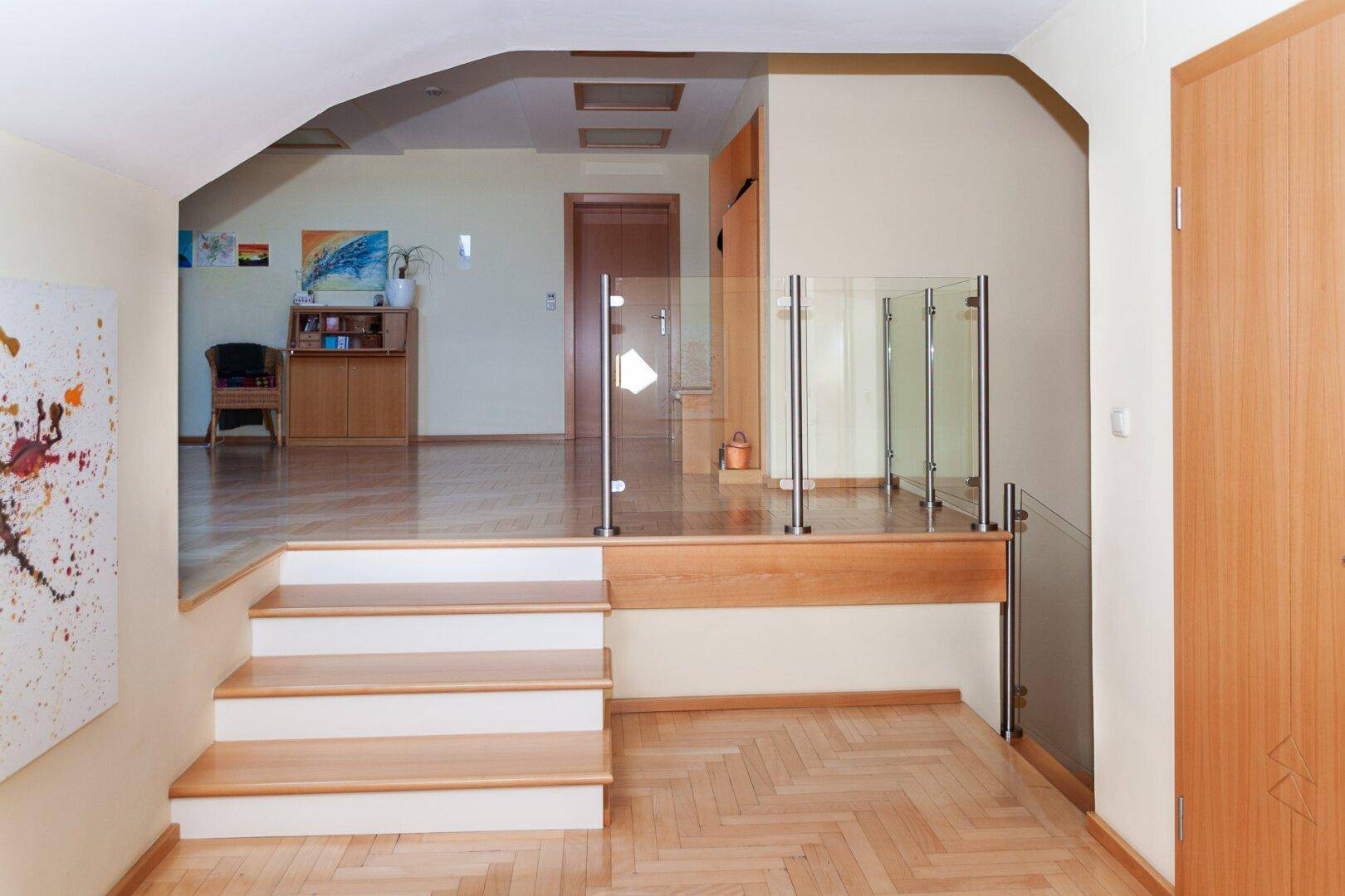 Heller Flur mit Treppe, Glasgeländer und Parkettboden, der verschiedene Ebenen verbindet.