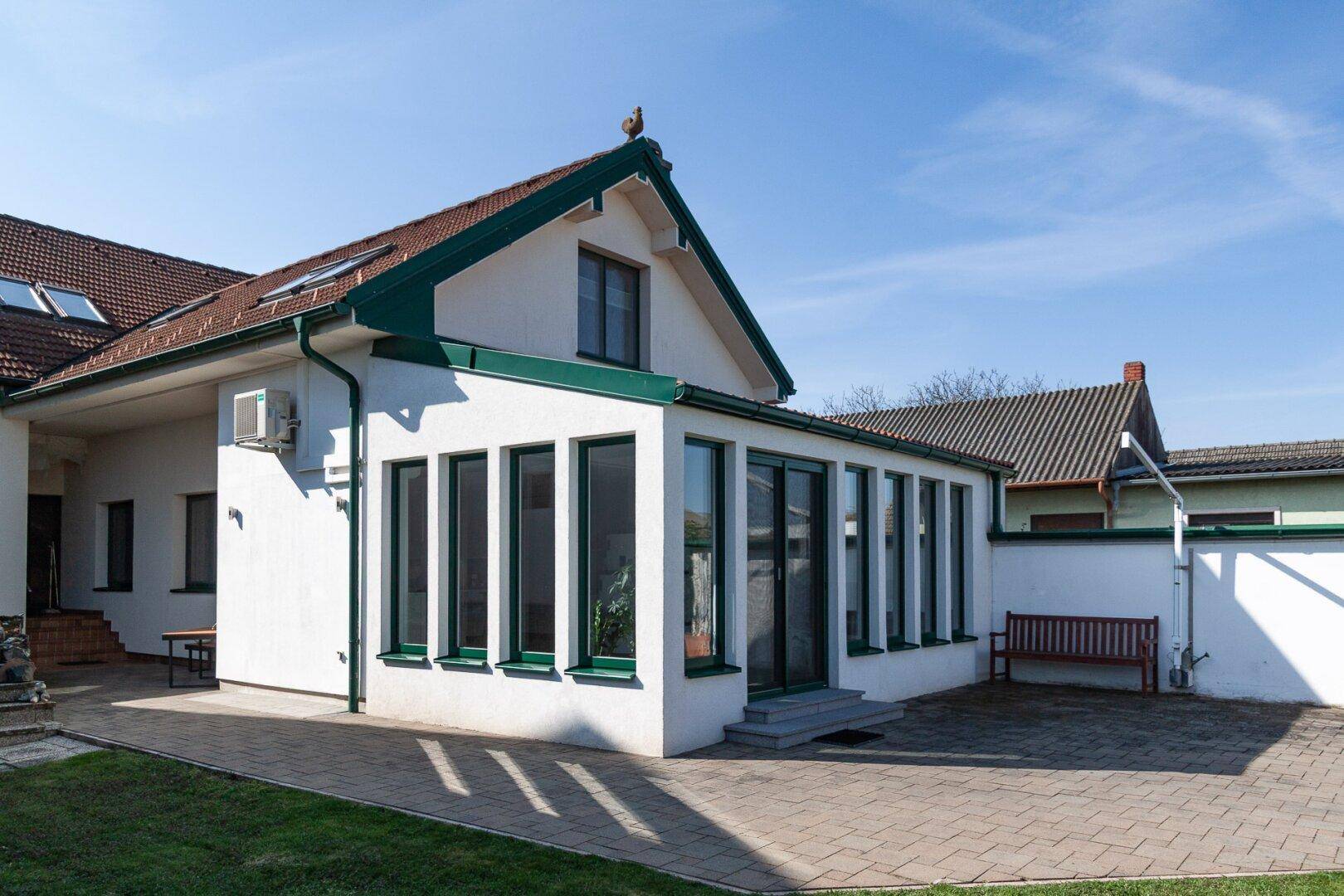 Haus mit Wintergarten und großer gepflasterter Terrasse, ideal für Outdoor-Aktivitäten.