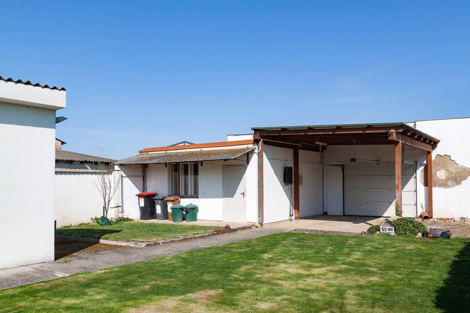 Nebengebäude mit Carport und Garage, umgeben von einer grünen Rasenfläche.