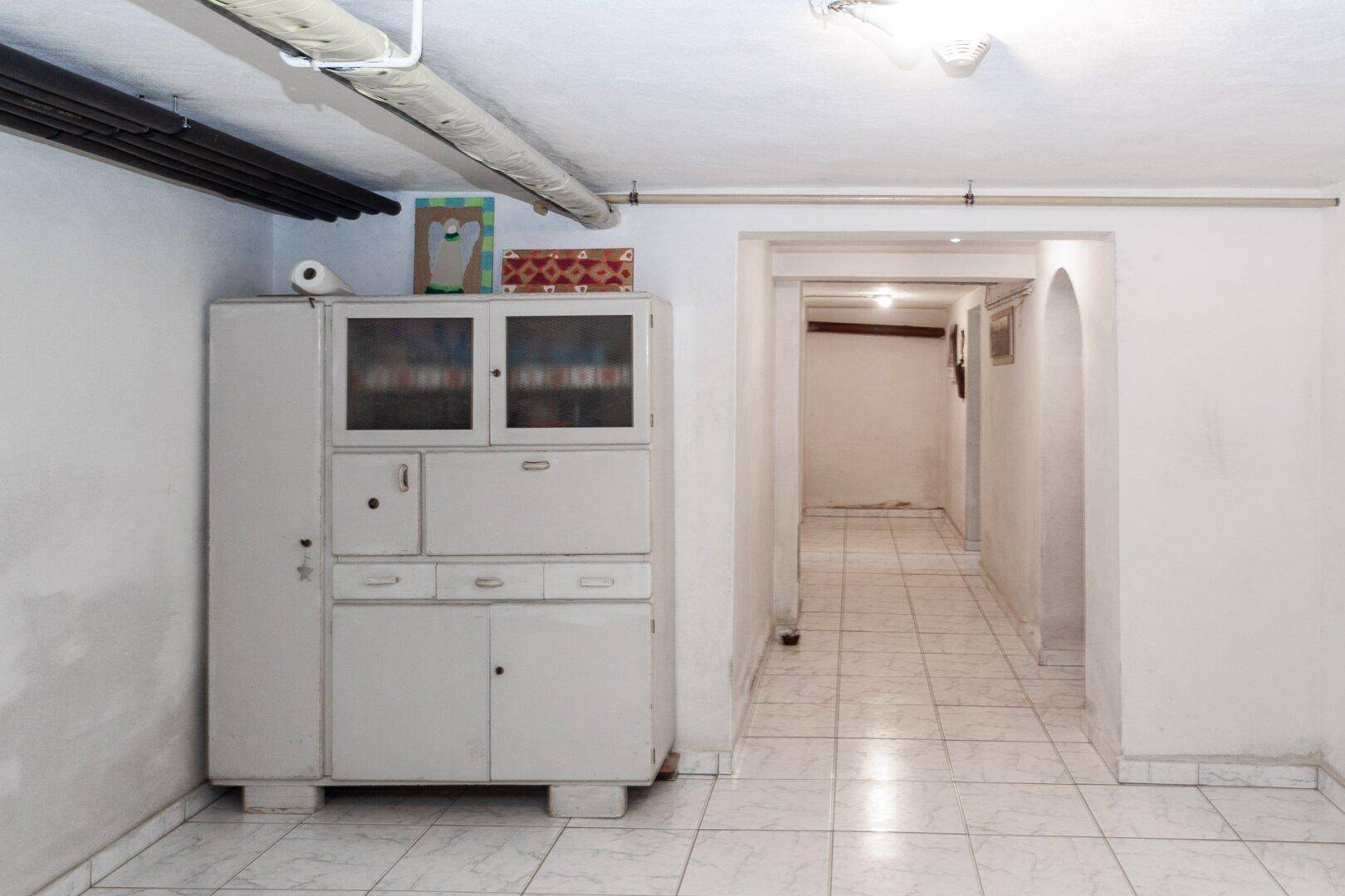 Kellerraum mit Fliesenboden und einem großen Schrank, bietet zusätzlichen Stauraum.