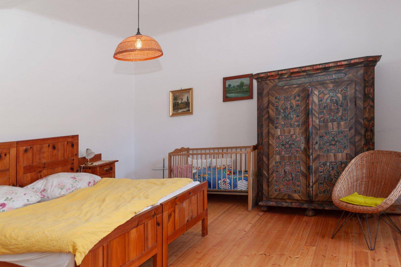 Geräumiges Schlafzimmer mit Holzboden, Doppelbett und traditionellem bemalten Schrank.