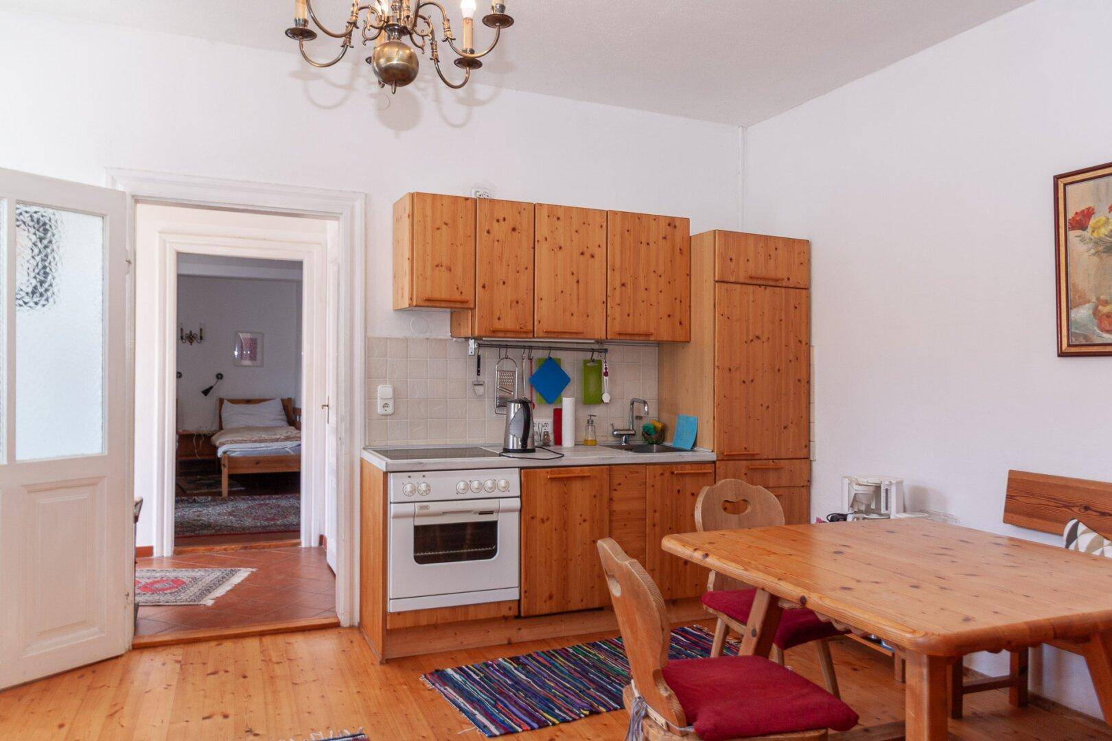 Wohnküche mit Holzküche, Esstisch und Blick in ein angrenzendes Schlafzimmer.