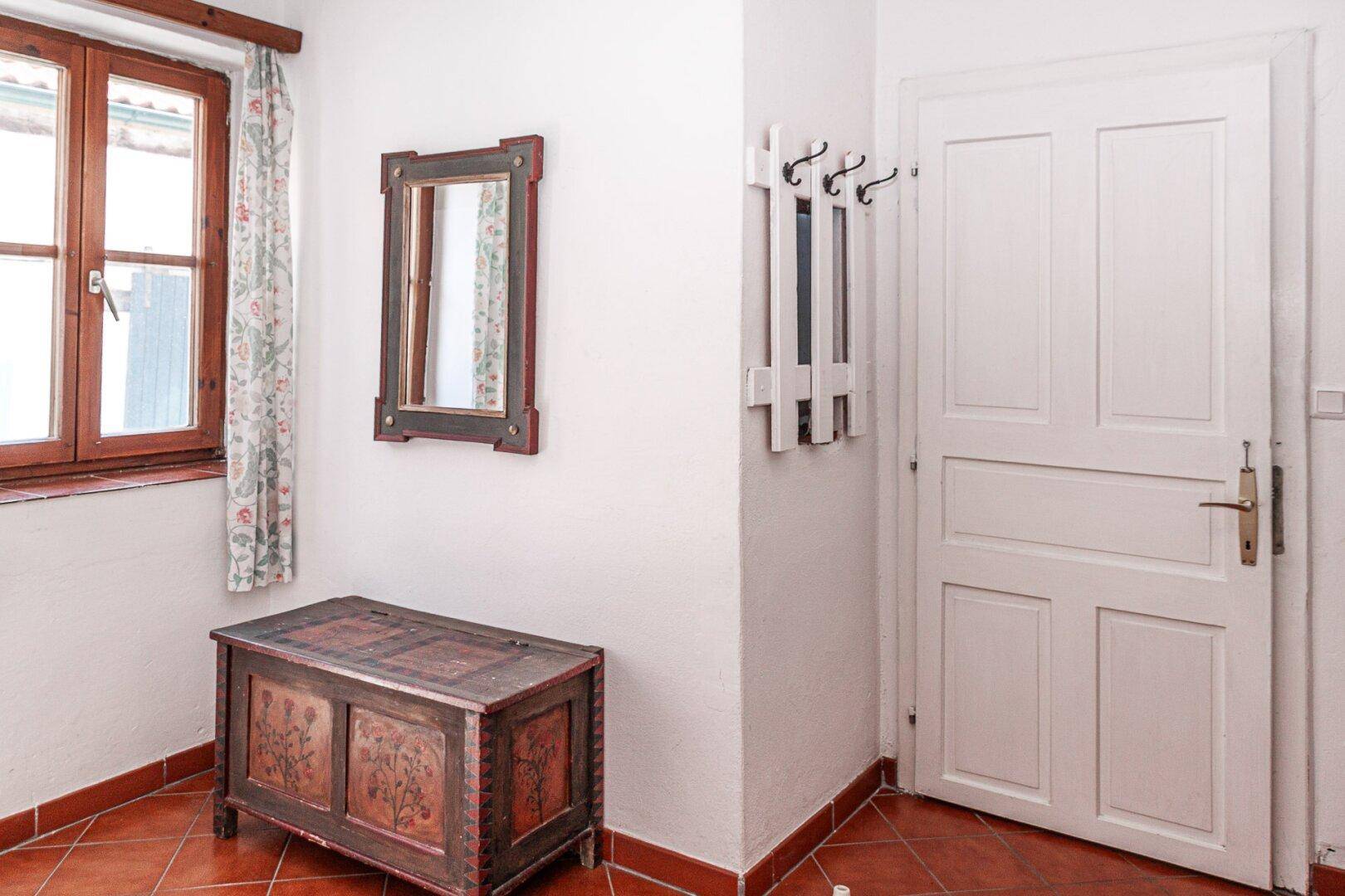 Heller Eingangsbereich mit Terrakotta-Fliesenboden, antiker Truhe und Garderobe.