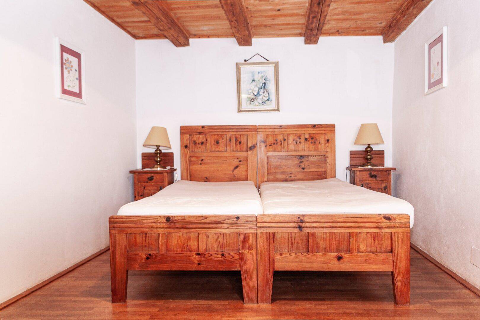 Gemütliches Schlafzimmer mit zwei Einzelbetten, Holzbalkendecke und rustikalem Holzfußboden.
