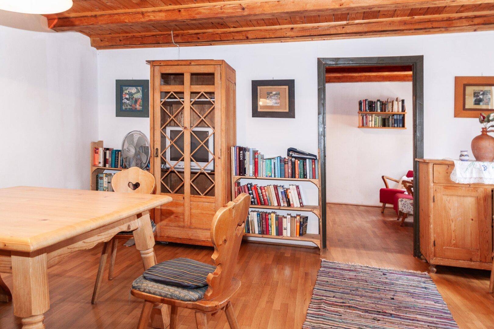 Wohn-Essbereich mit Holztisch, Bücherregalen und einer rustikalen Holzbalkendecke.