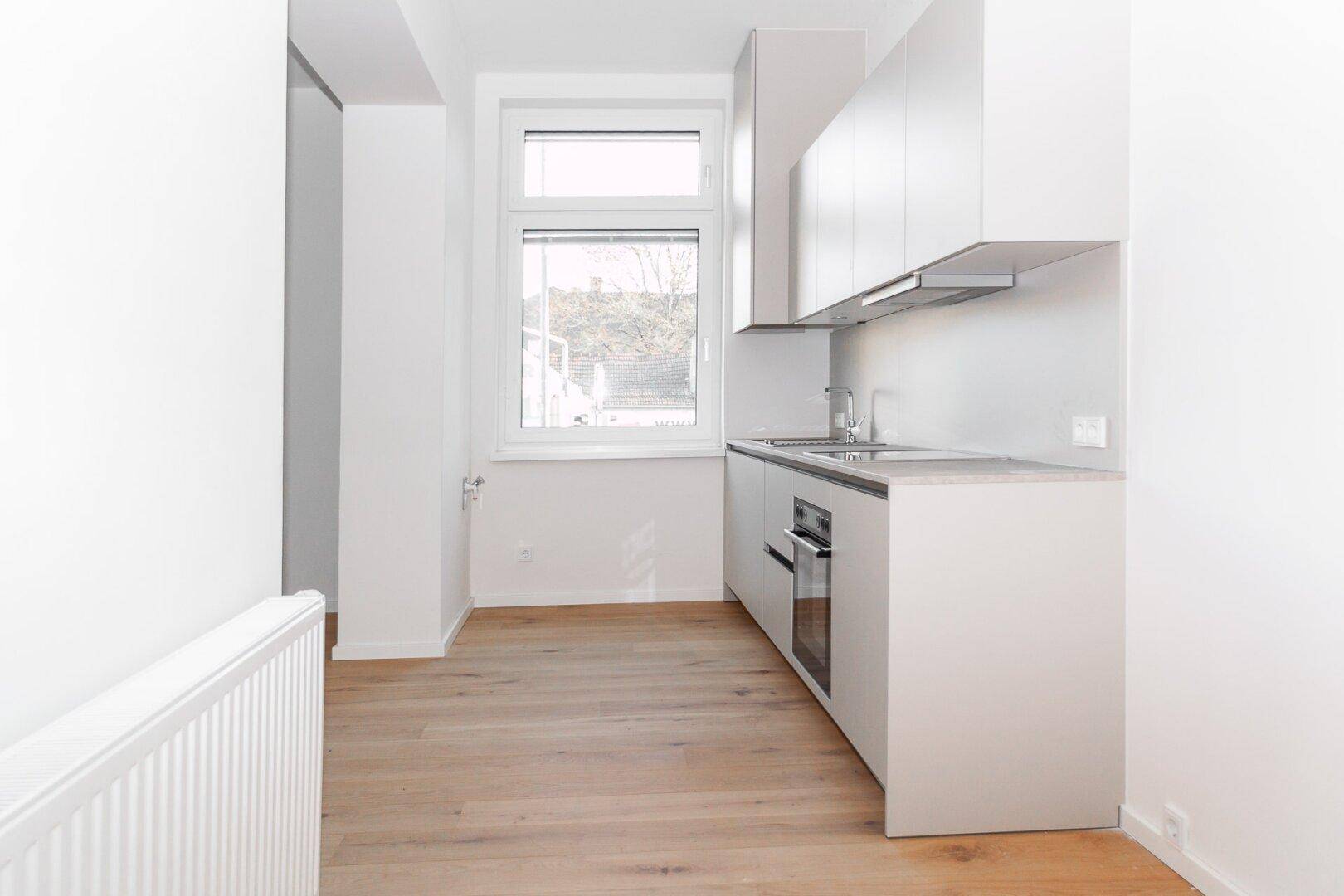 Funktionale Küche mit hellgrauen Schränken, Holzfußboden und Fenster für natürliche Belichtung.
