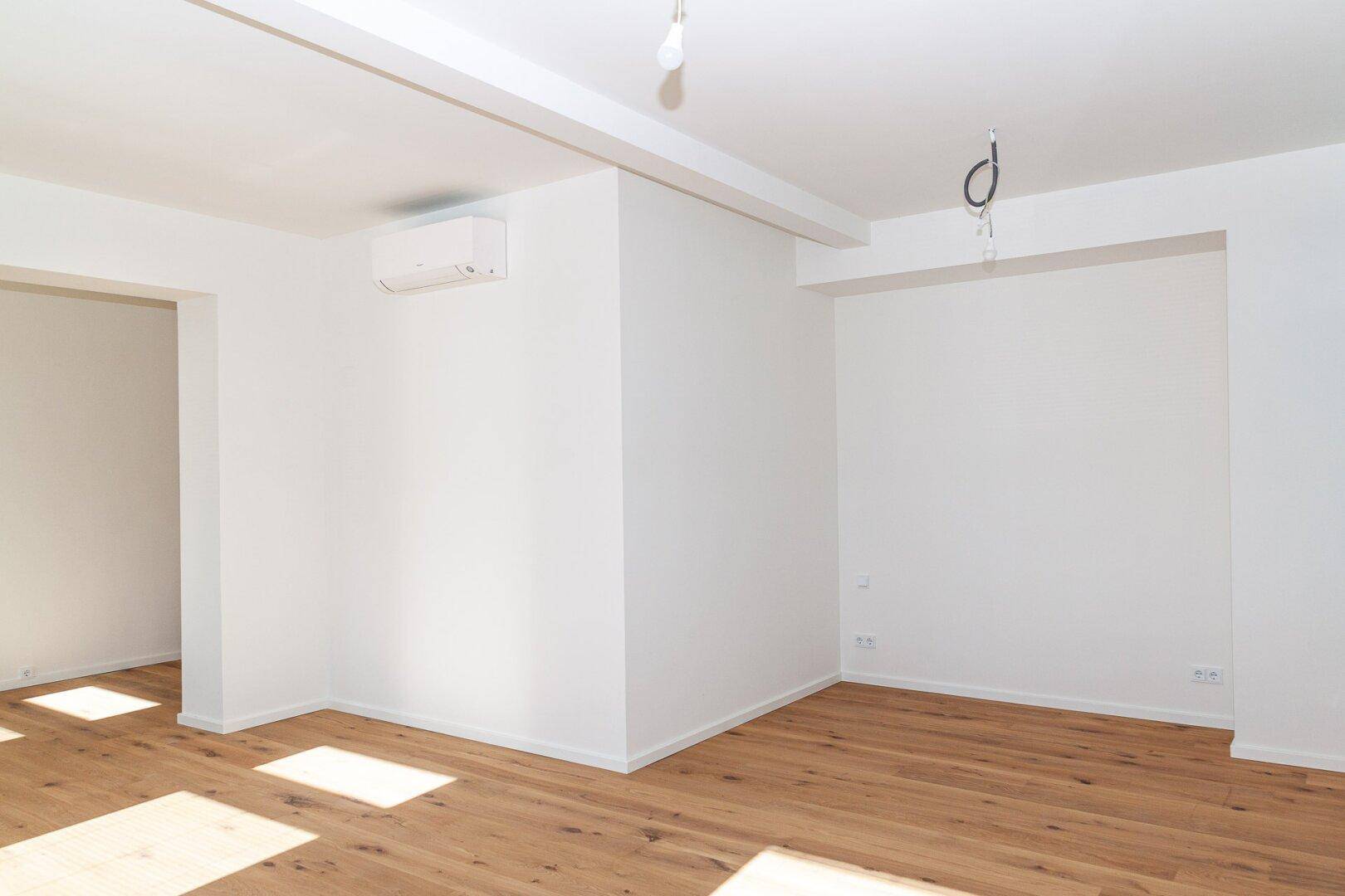 Geräumiger Wohnbereich mit Holzfußboden, Klimaanlage und viel Tageslicht.