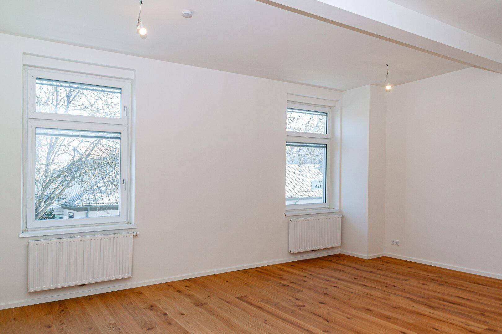 Lichtdurchflutetes Zimmer mit Parkettboden und zwei Fenstern, bietet viel Potenzial für Einrichtungsideen.