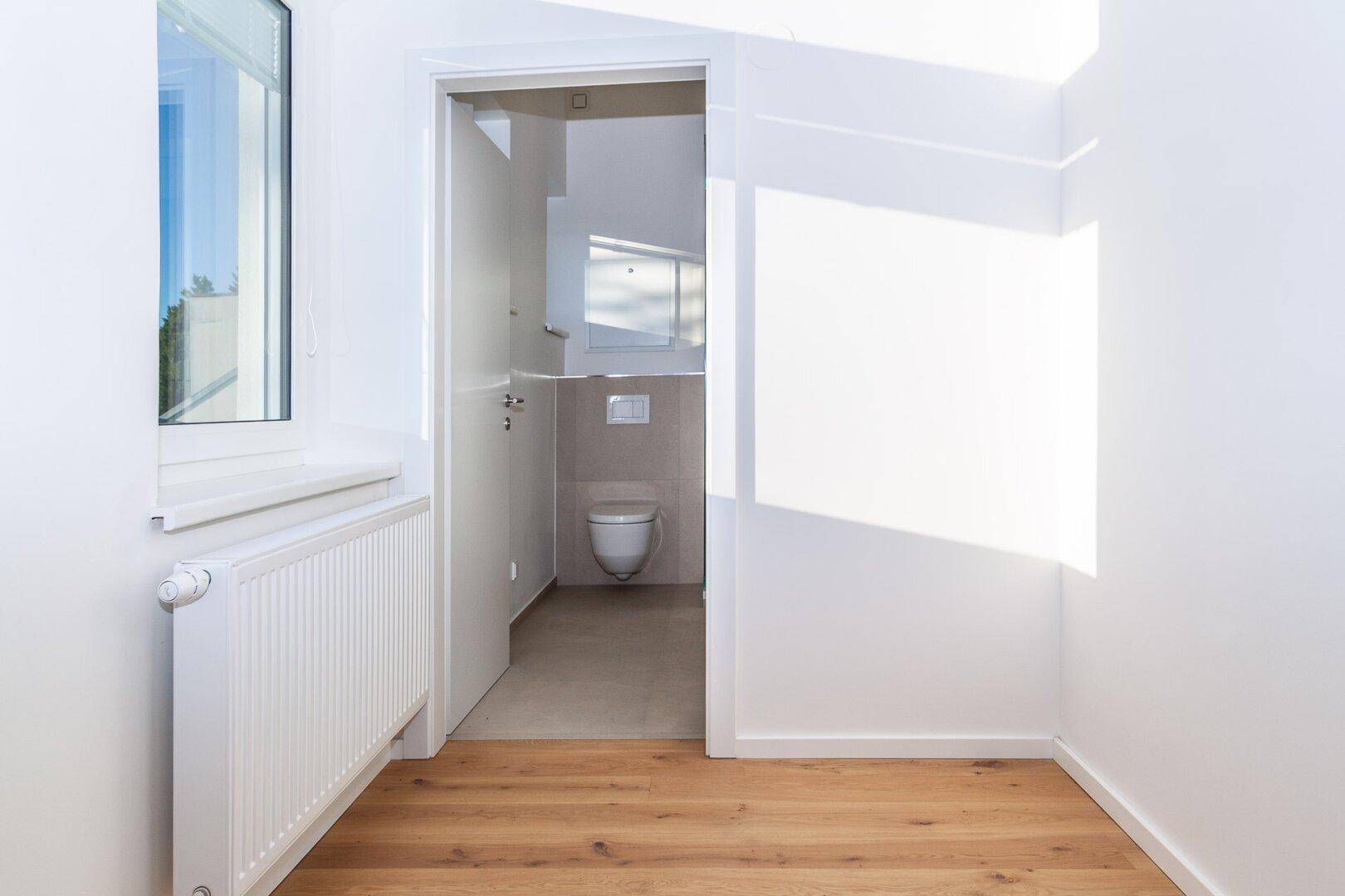 Heller Flur mit Holzboden und Zugang zu einem separaten WC, gut beleuchtet durch ein Fenster.