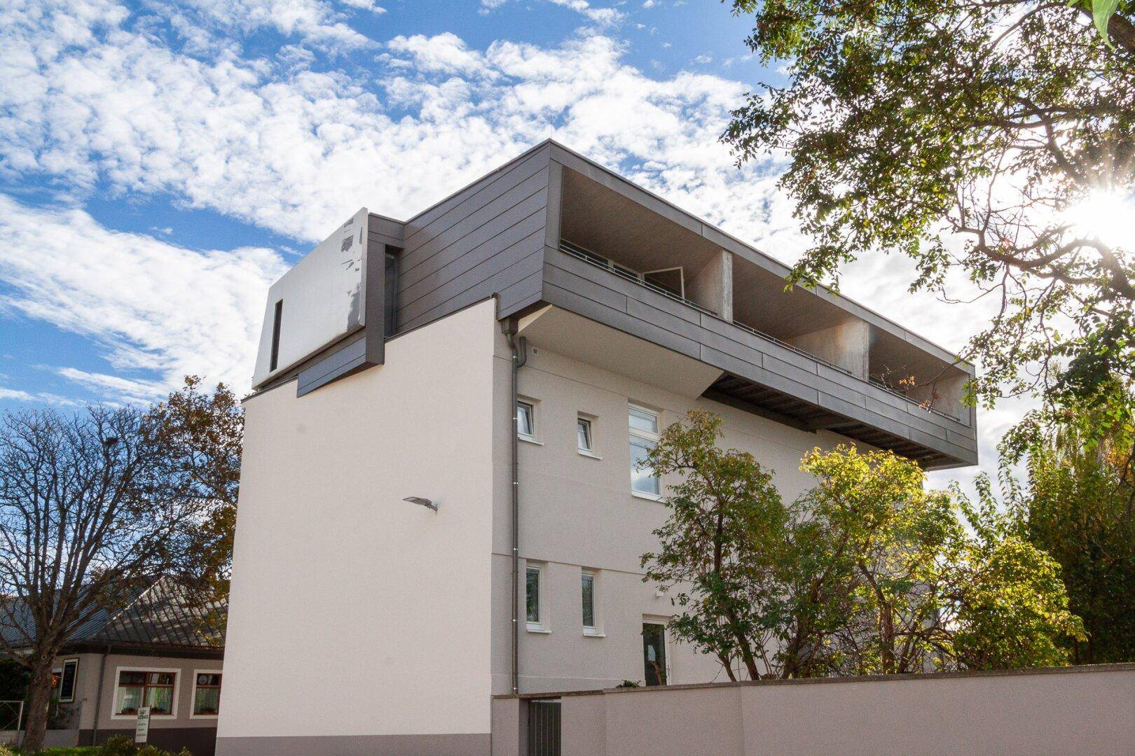 Zeitgenössisches Gebäude mit großen Balkonen und einer hellen Fassade unter blauem Himmel.
