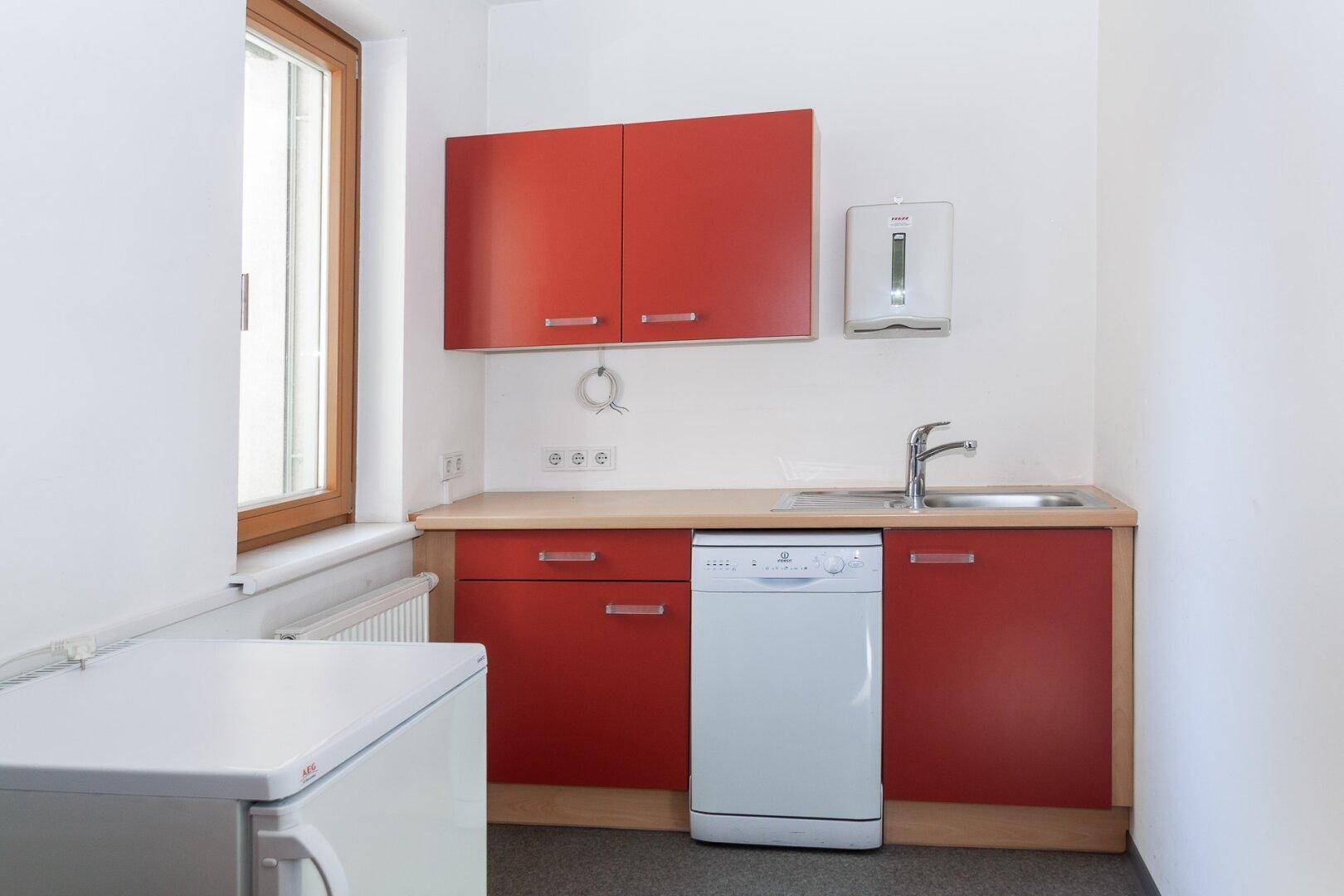 Kleine Küchenzeile mit roten Schränken, Spüle, Geschirrspüler und Fenster.